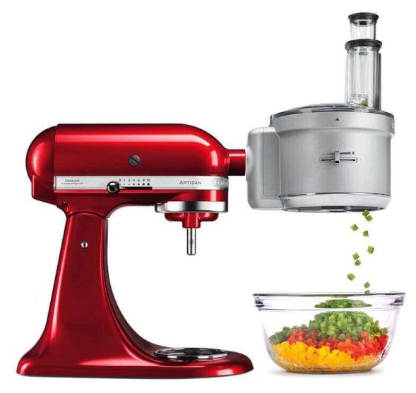 Egy piros KitchenAid álló mixer ezüst színű robotgép feltéttel, zöldségeket aprít egy tálba.