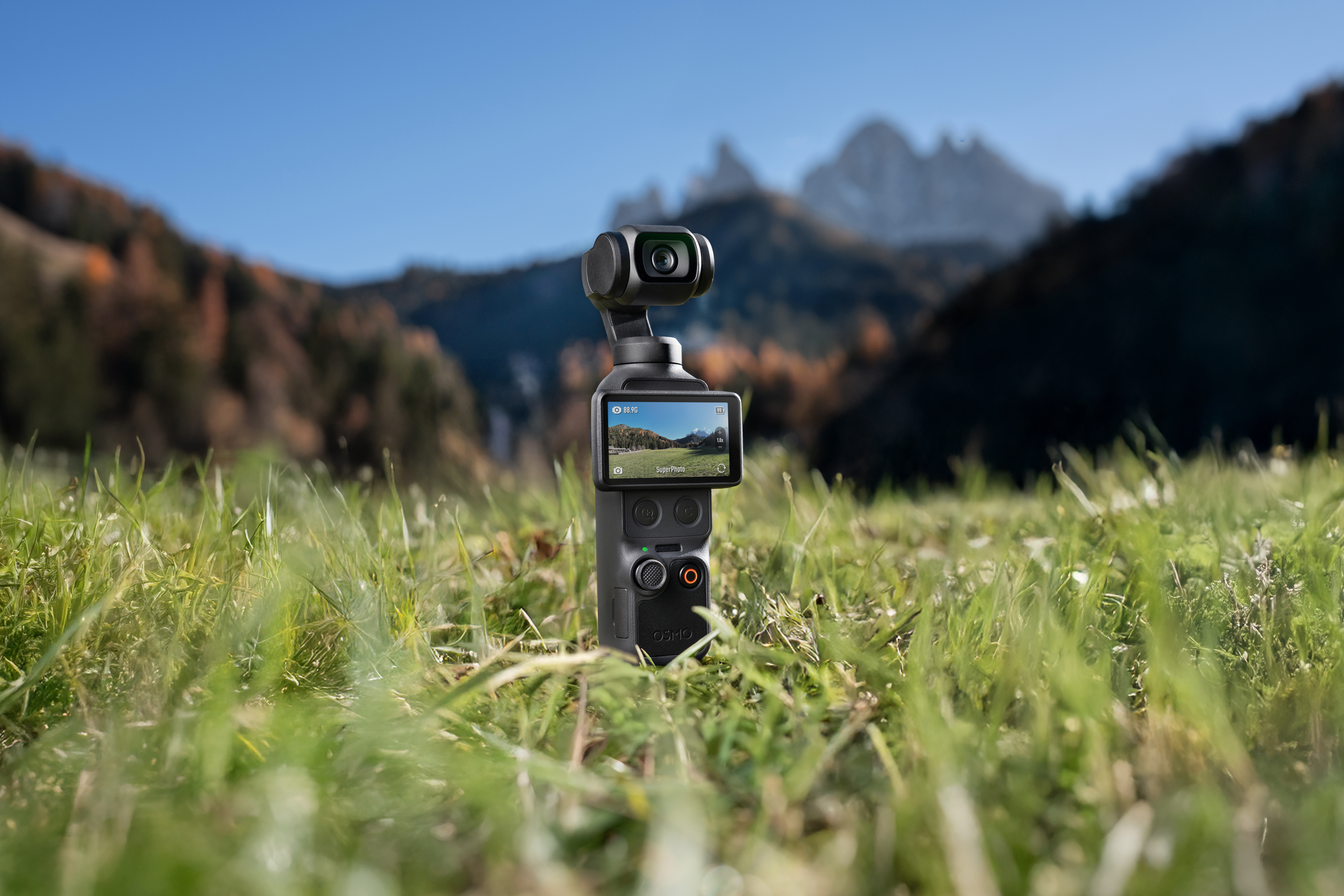 Ein Gimbal-Kamera-Gerät steht im Gras mit Berglandschaft im Hintergrund.