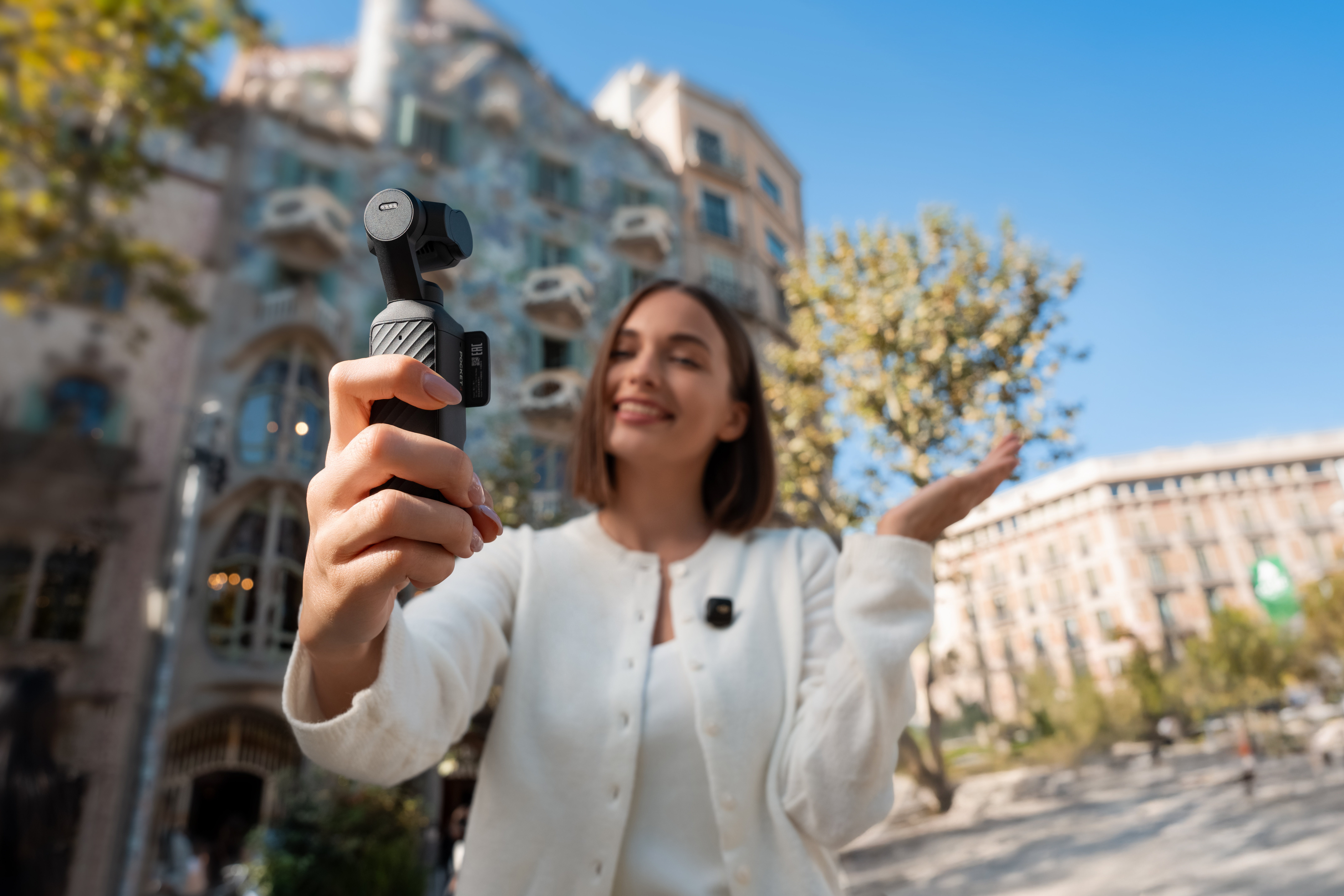 Eine Frau filmt sich mit einem Gimbal vor einem Gebäude. Sie trägt eine weiße Strickjacke.