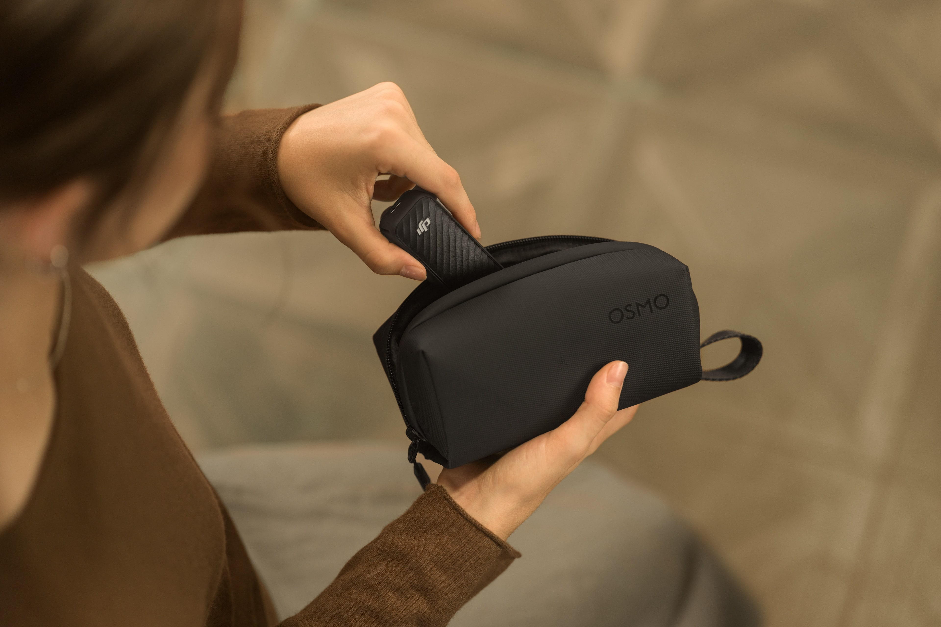 Eine Hand legt einen schwarzen Gimbal in eine schwarze OSMO-Tasche.