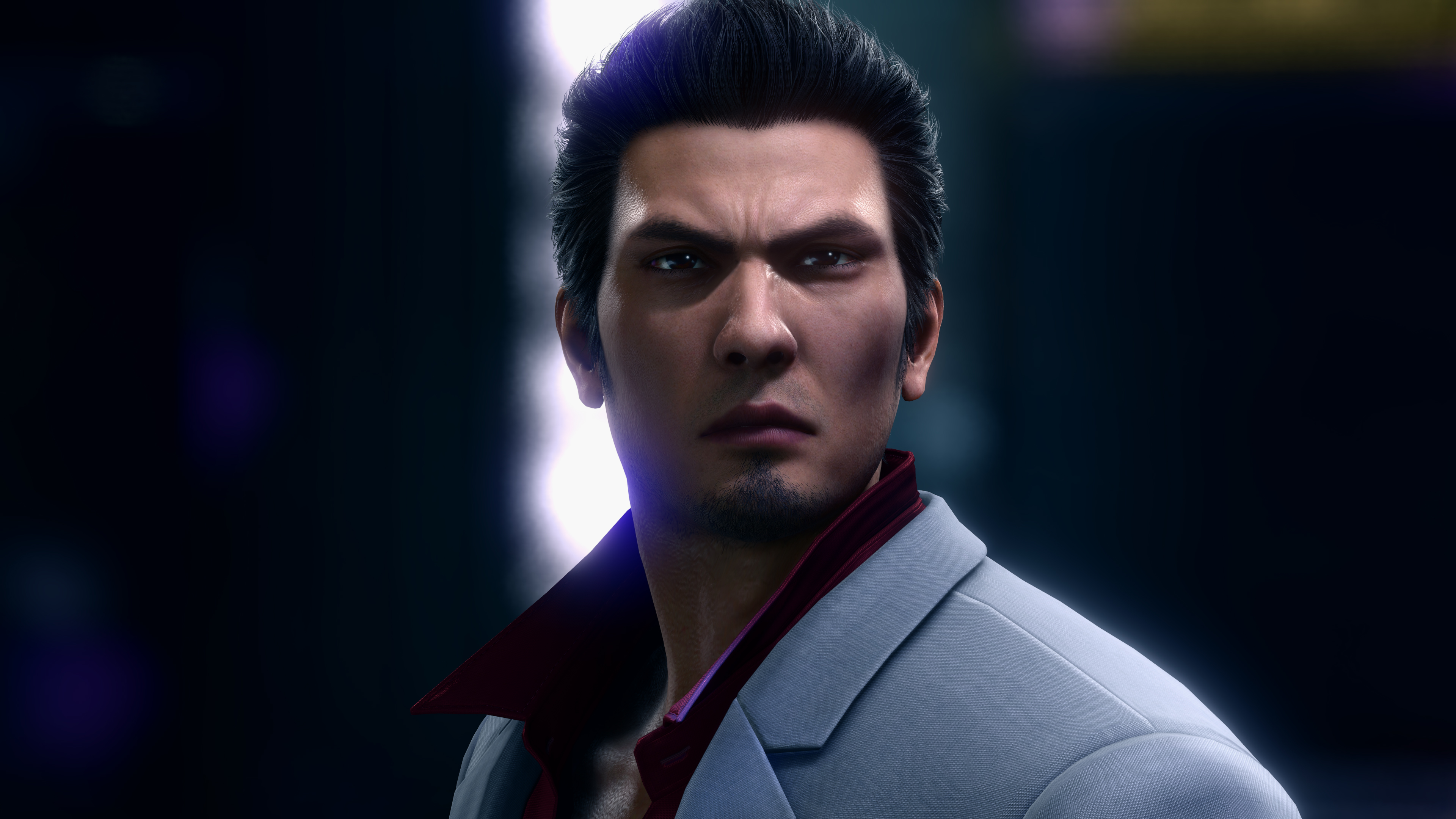 Un uomo con capelli scuri indossa un abito grigio chiaro e una camicia rosso scuro.