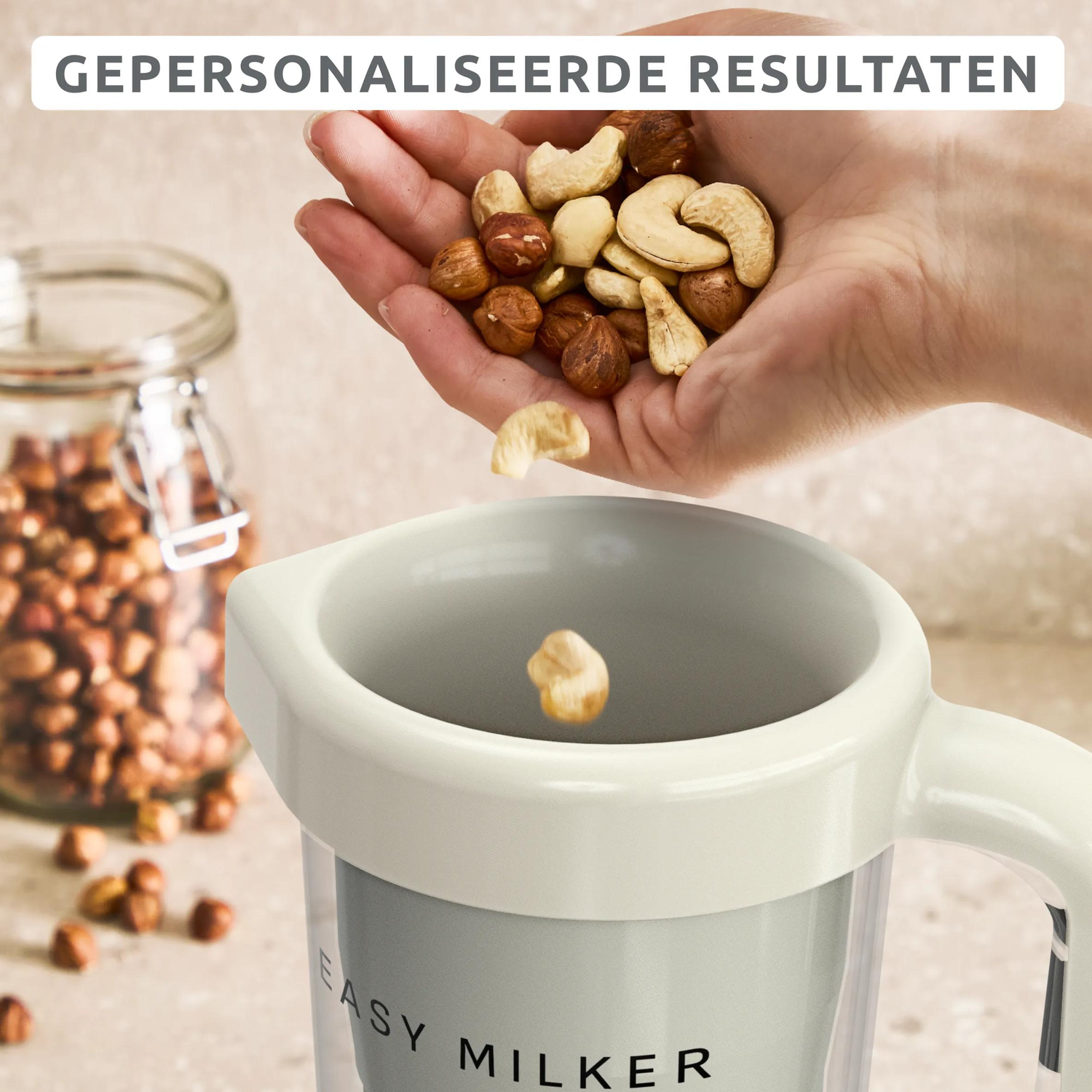 Een hand giet noten in een mixer. Op de achtergrond een glazen pot met noten.
