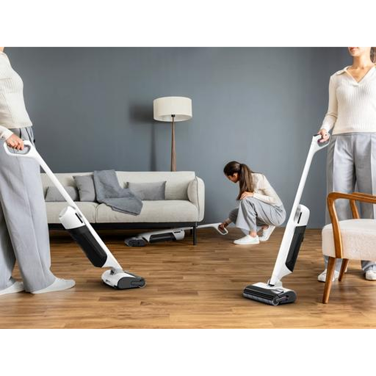 Three people vacuuming a wooden floor in a living room setting.