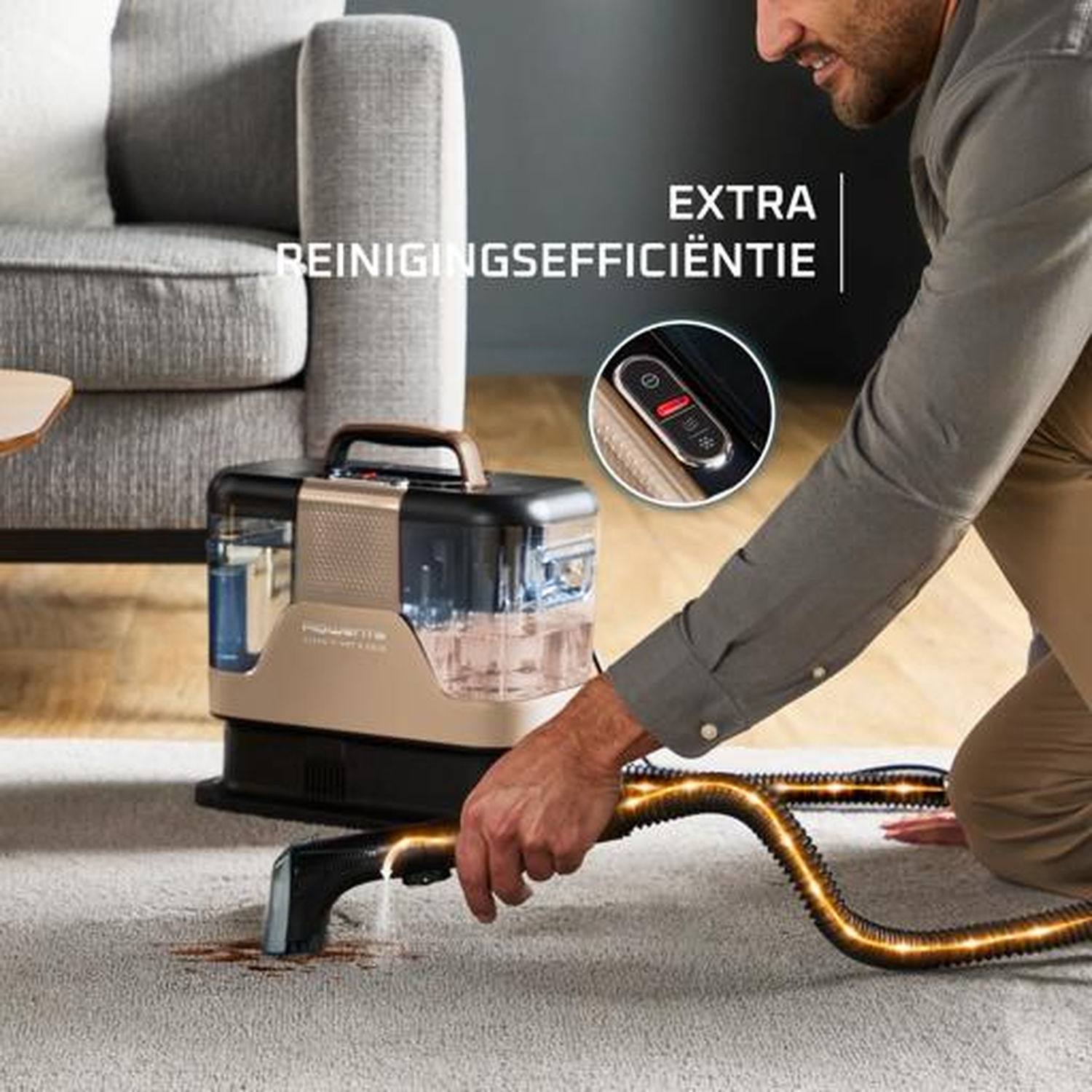 Man cleans carpet with a device, sofa in the background.