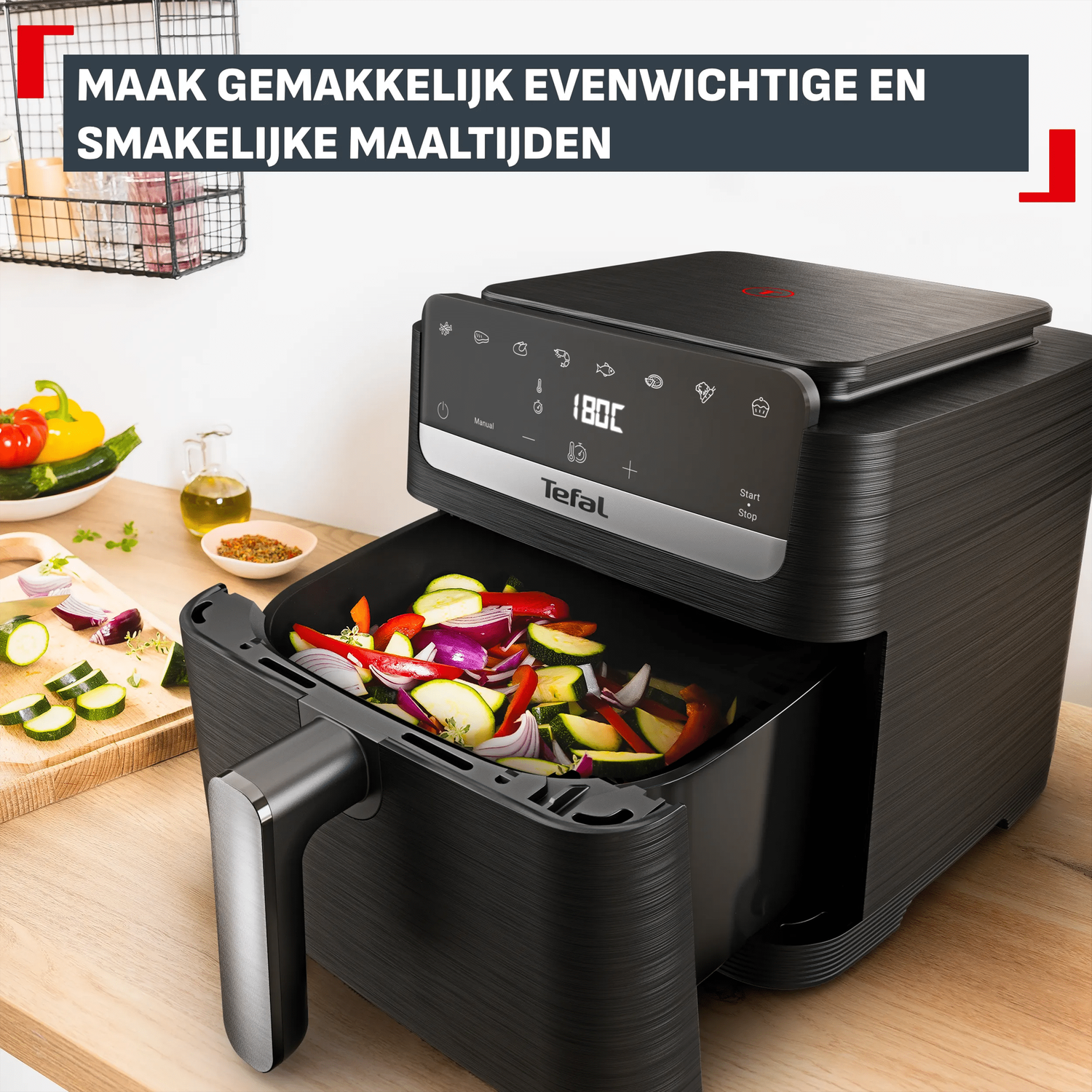 Zwarte heteluchtfriteuse gevuld met groenten, naast ingrediënten op een houten plank.