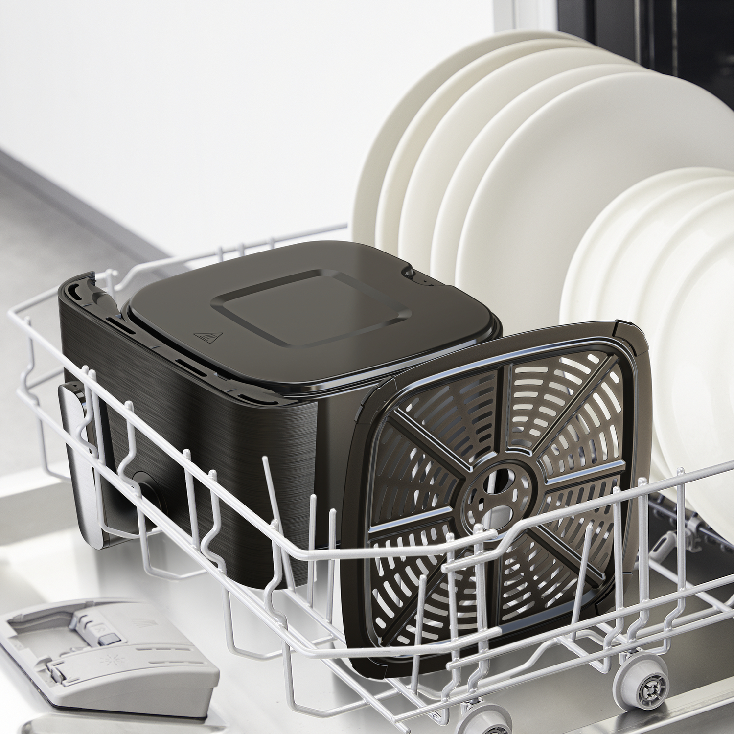 Een zwarte airfryer mand en deksel in een vaatwasrek met witte borden.