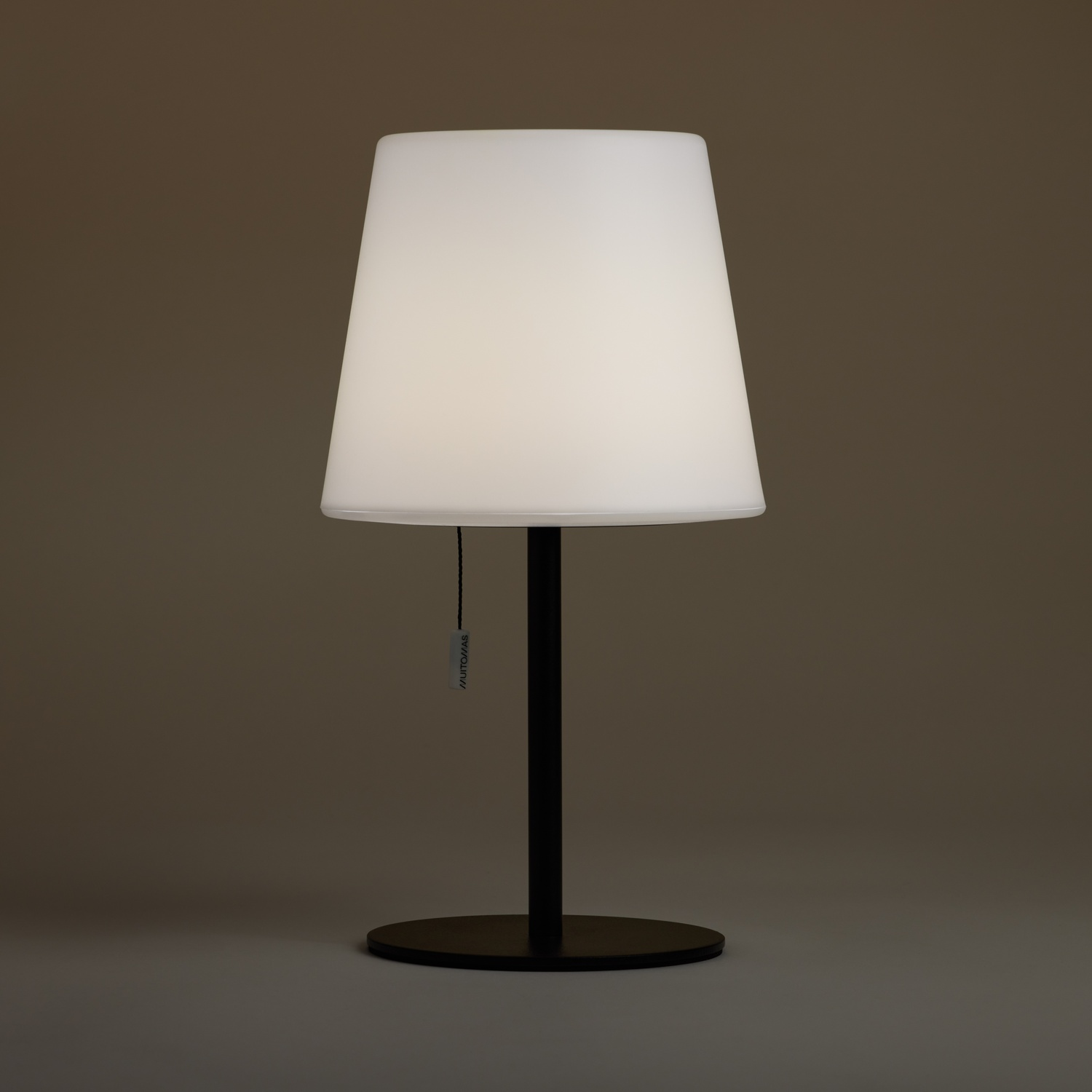 Una lampada da terra bianca con paralume e stelo nero è su un pavimento grigio.