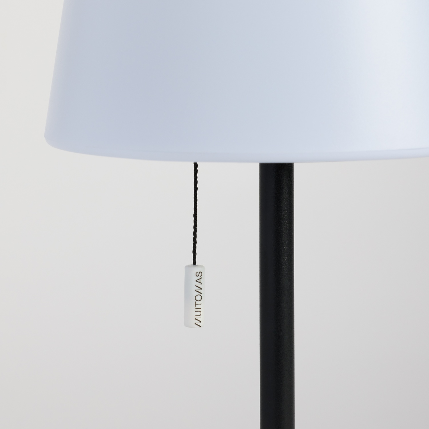 Primo piano di una lampada da terra con paralume bianco, stelo nero e cordina.