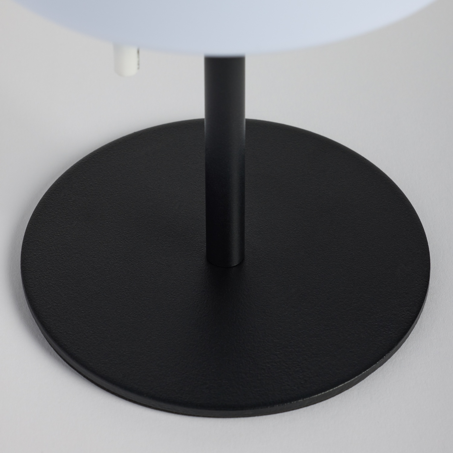 Base rotonda nera per lampada con un palo scuro e un componente bianco.