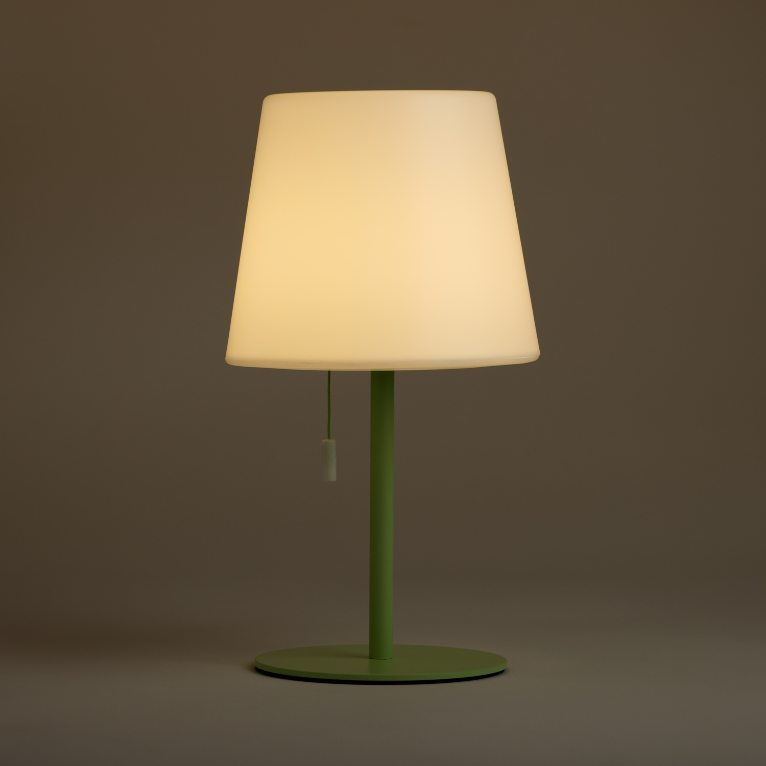 Una lampada bianca con stelo e base verdi si erge su uno sfondo grigio.