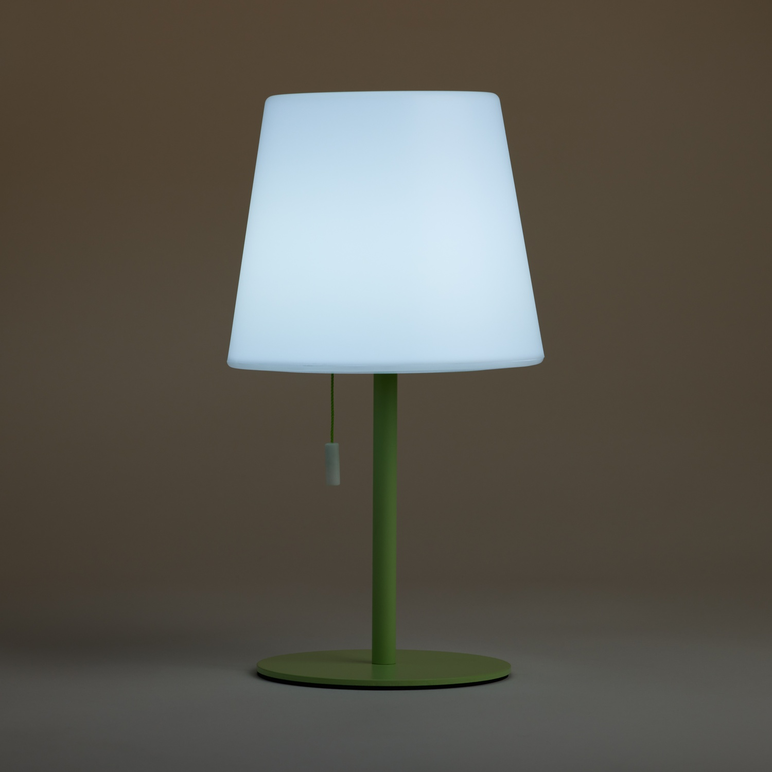 Lampada bianca luminosa con base verde su superficie grigia.