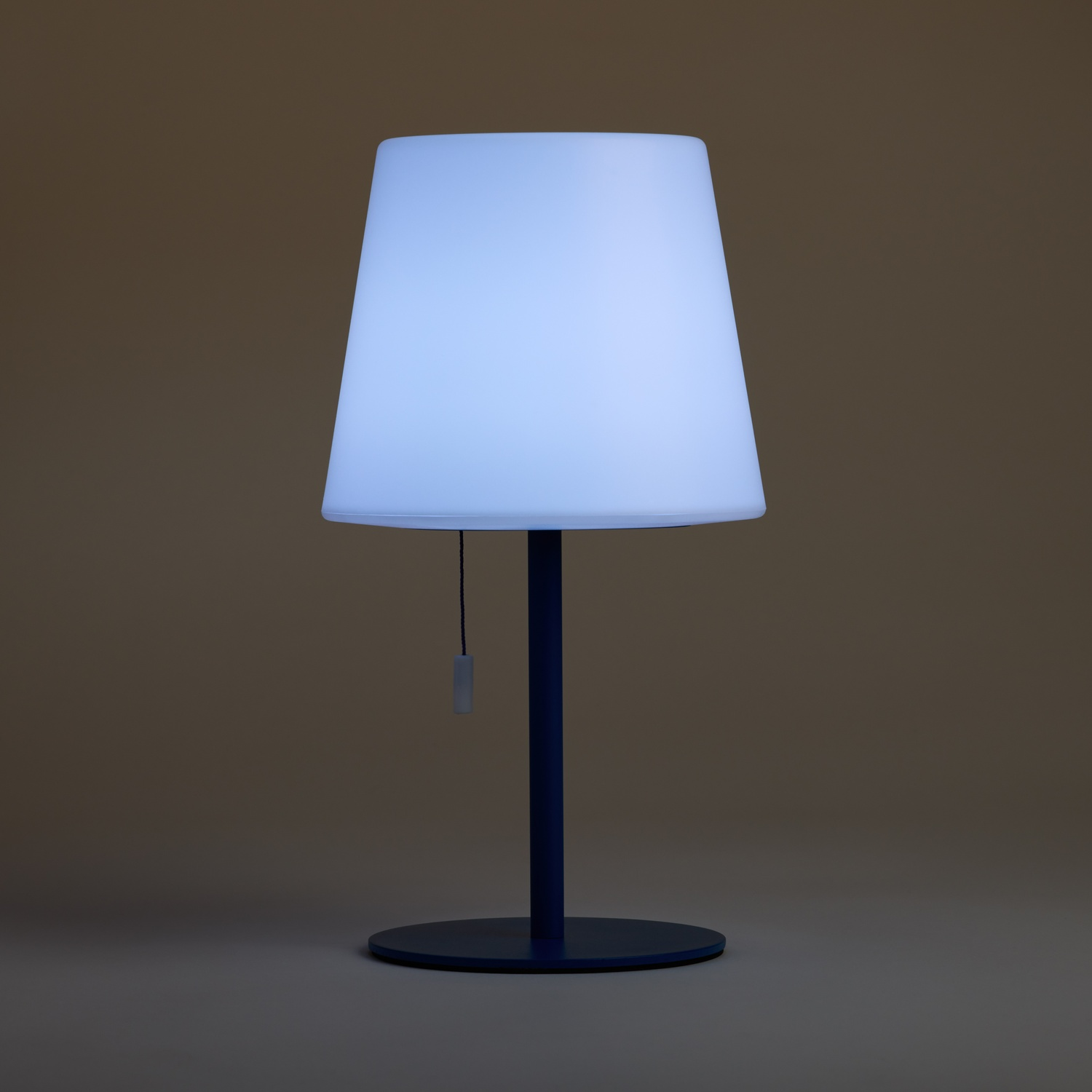Una lampada da terra blu con paralume bianco illuminato si erge su una base rotonda.