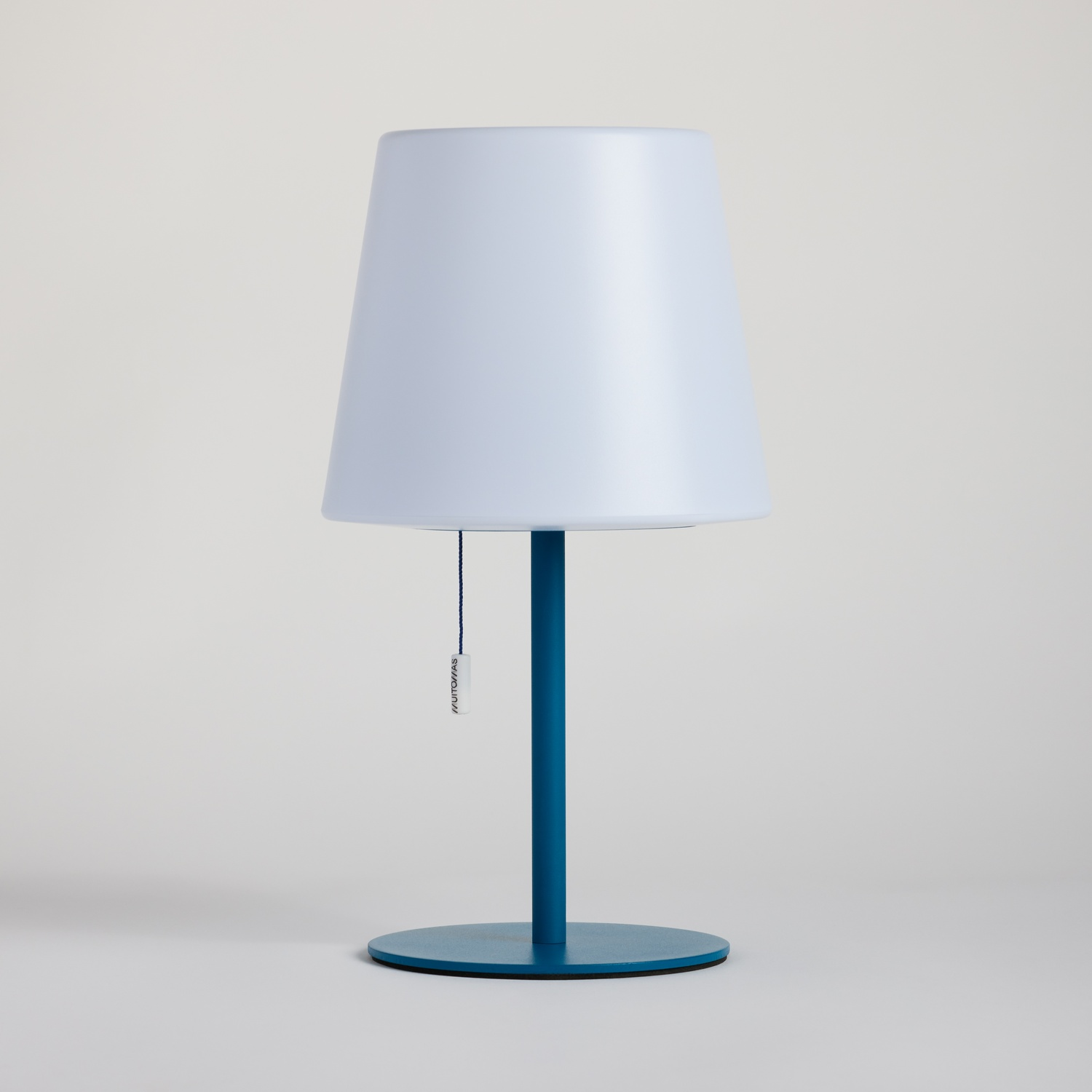 Una lampada da terra blu con paralume bianco si erge su sfondo chiaro.