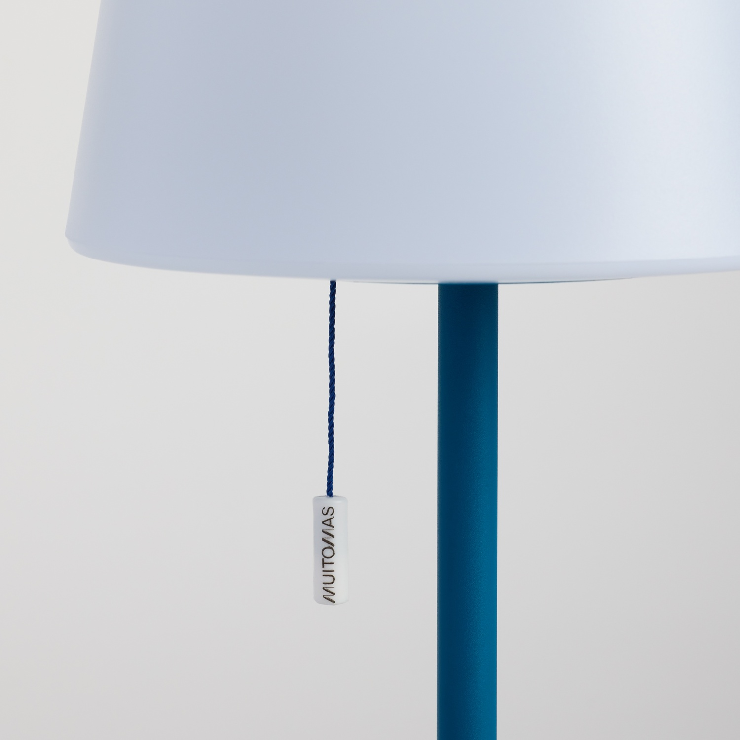 Un supporto per lampada blu con paralume bianco e cordino di trazione blu.
