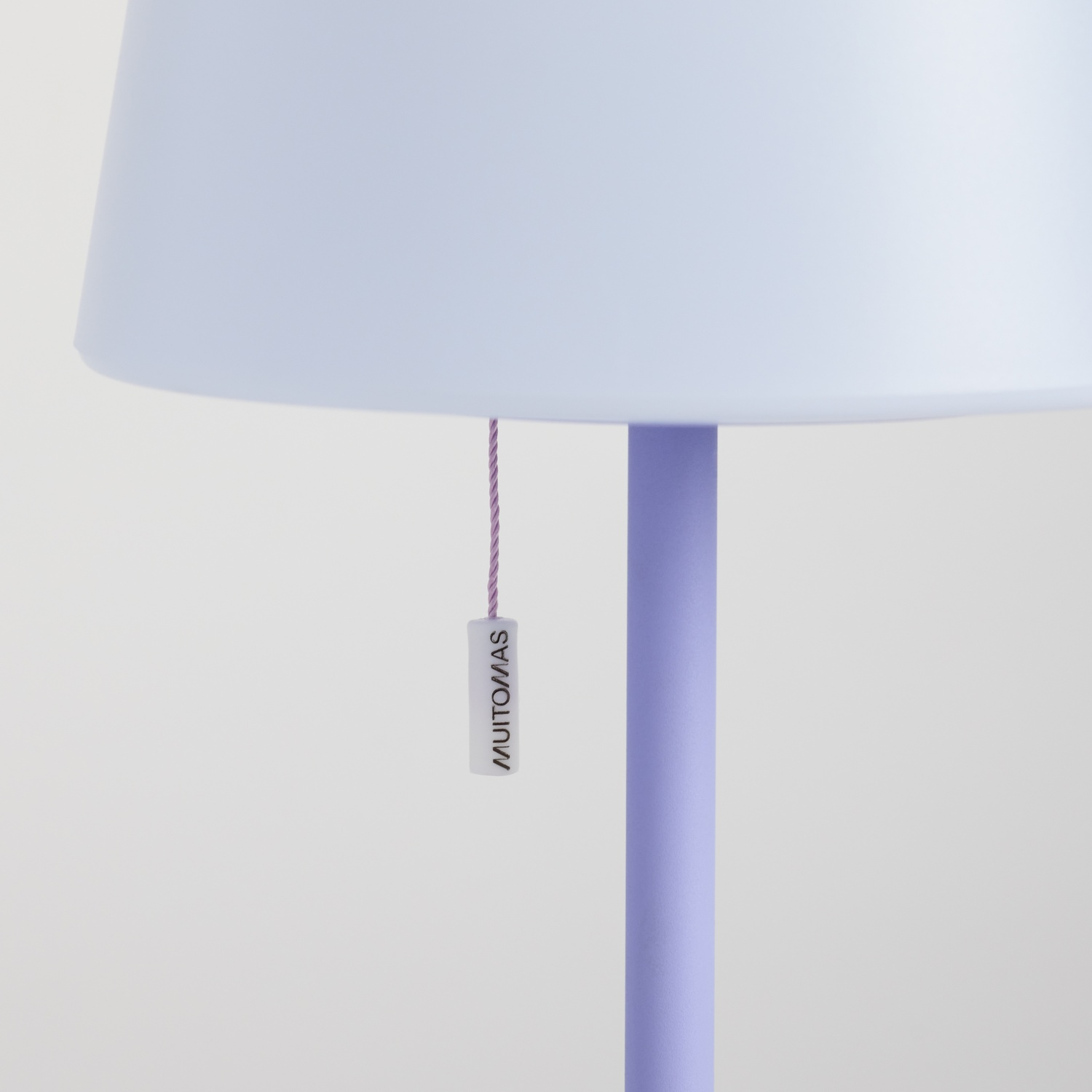 Lampada da terra viola con paralume bianco e piccolo cartellino con scritto MUITOMAS.