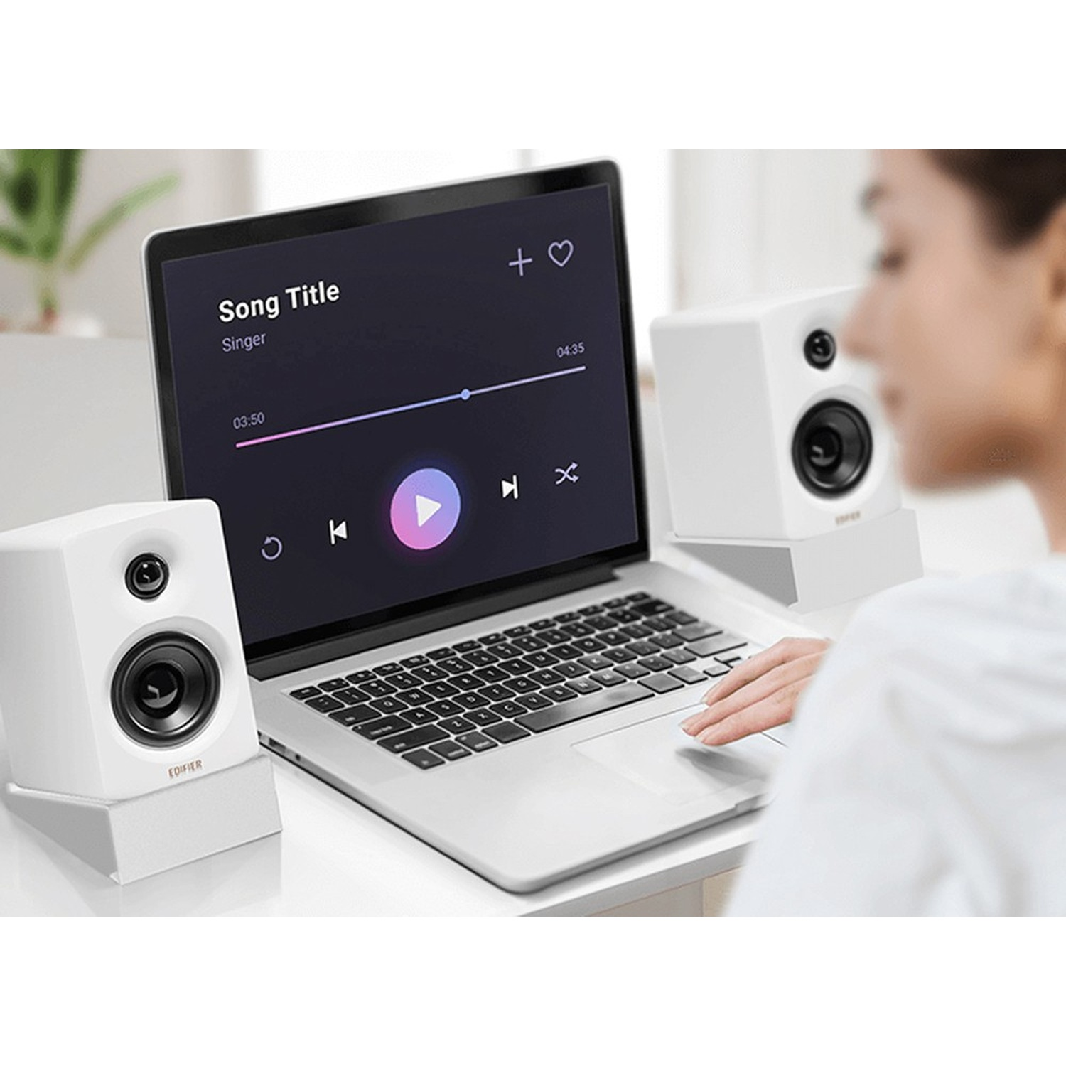 Un laptop con app musicale, due altoparlanti bianchi e una persona.