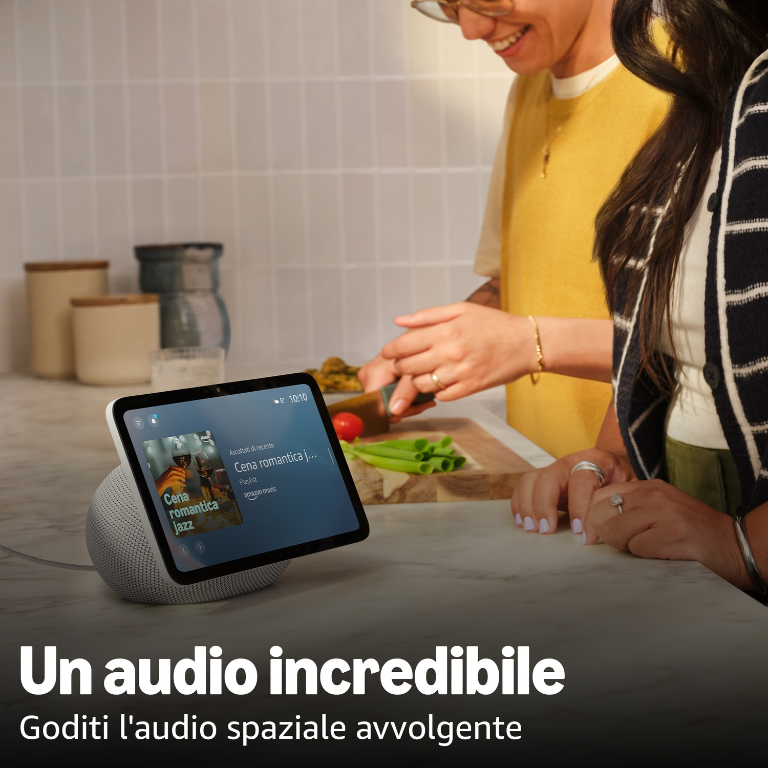 Uno smart speaker grigio con tablet che riproduce musica. Due persone sullo sfondo.