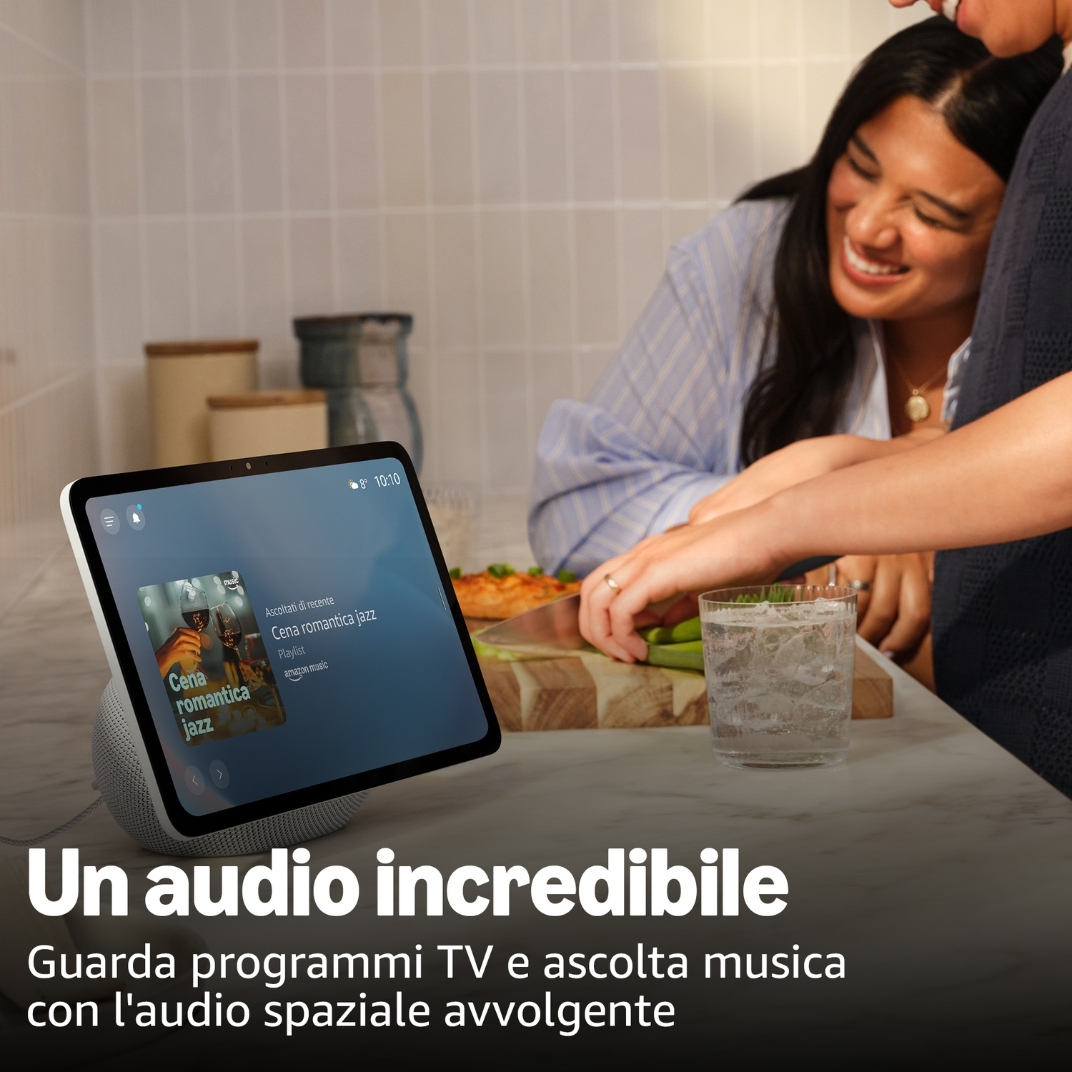 Un uomo e una donna ridono vicino a un altoparlante intelligente con schermo musicale.