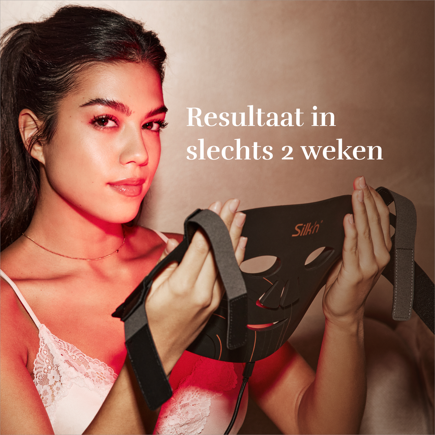 Vrouw houdt een zwart gezichtsmasker met rode lichten vast, zittend bij een raam.