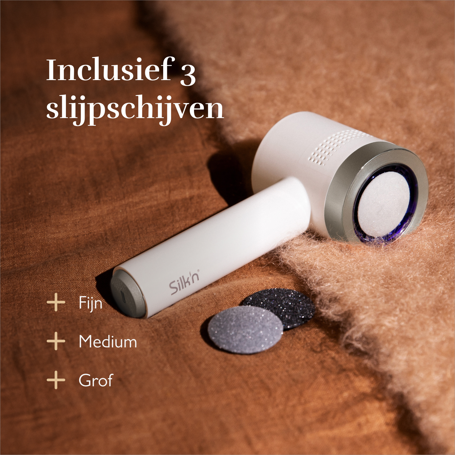 A white skincare device with three sanding discs on a brown fabric.