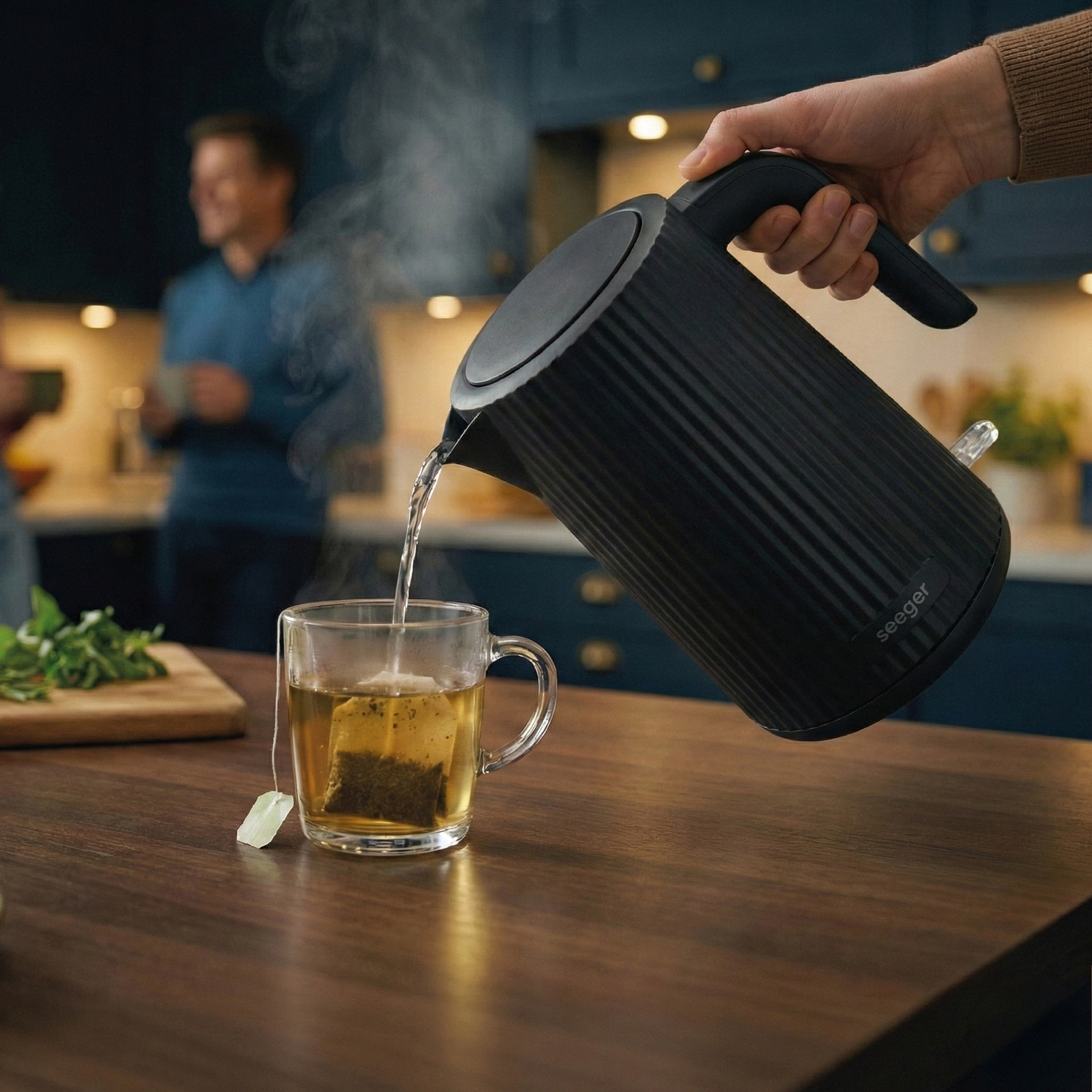 Heet water wordt uit een zwarte waterkoker in een theekopje met theezakje gegoten.