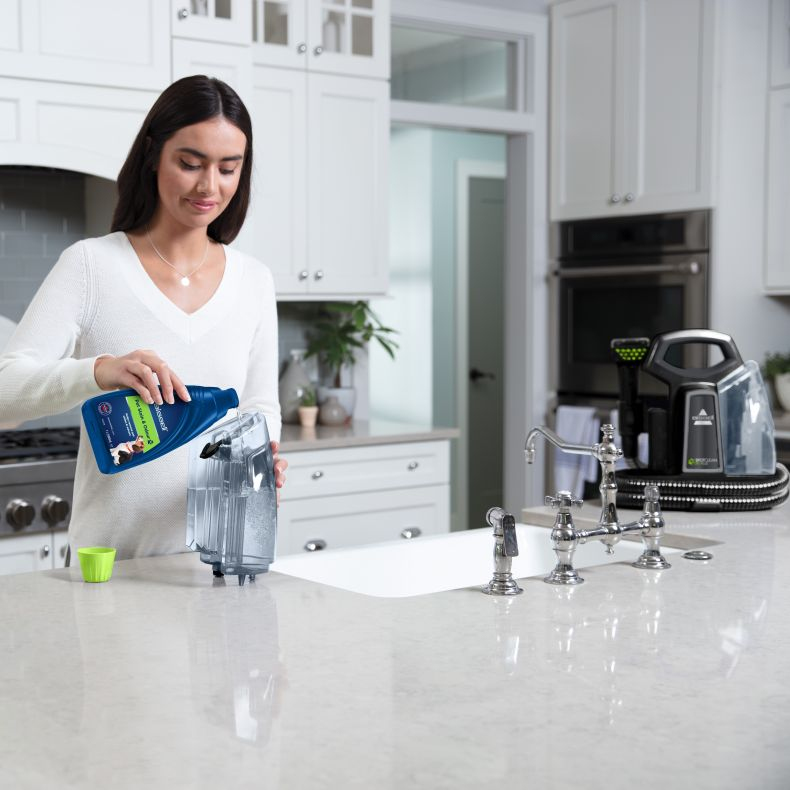 Una mujer vierte líquido azul en un tanque de agua en una cocina.