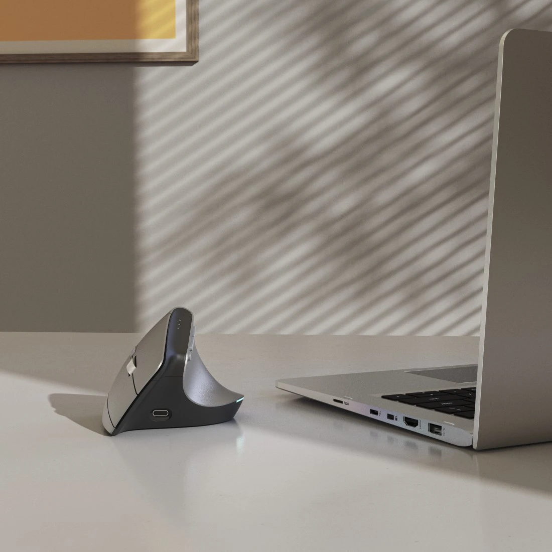 Ergonomiczna mysz i laptop na biurku oświetlone światłem z okna.
