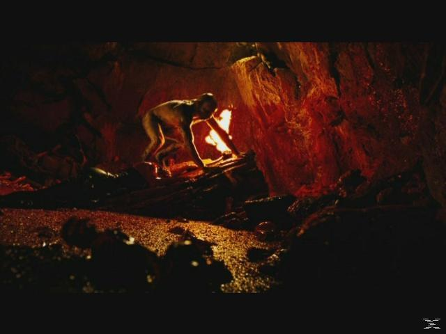 Ein Wesen kauert sich in einer Höhle neben einem Feuer.