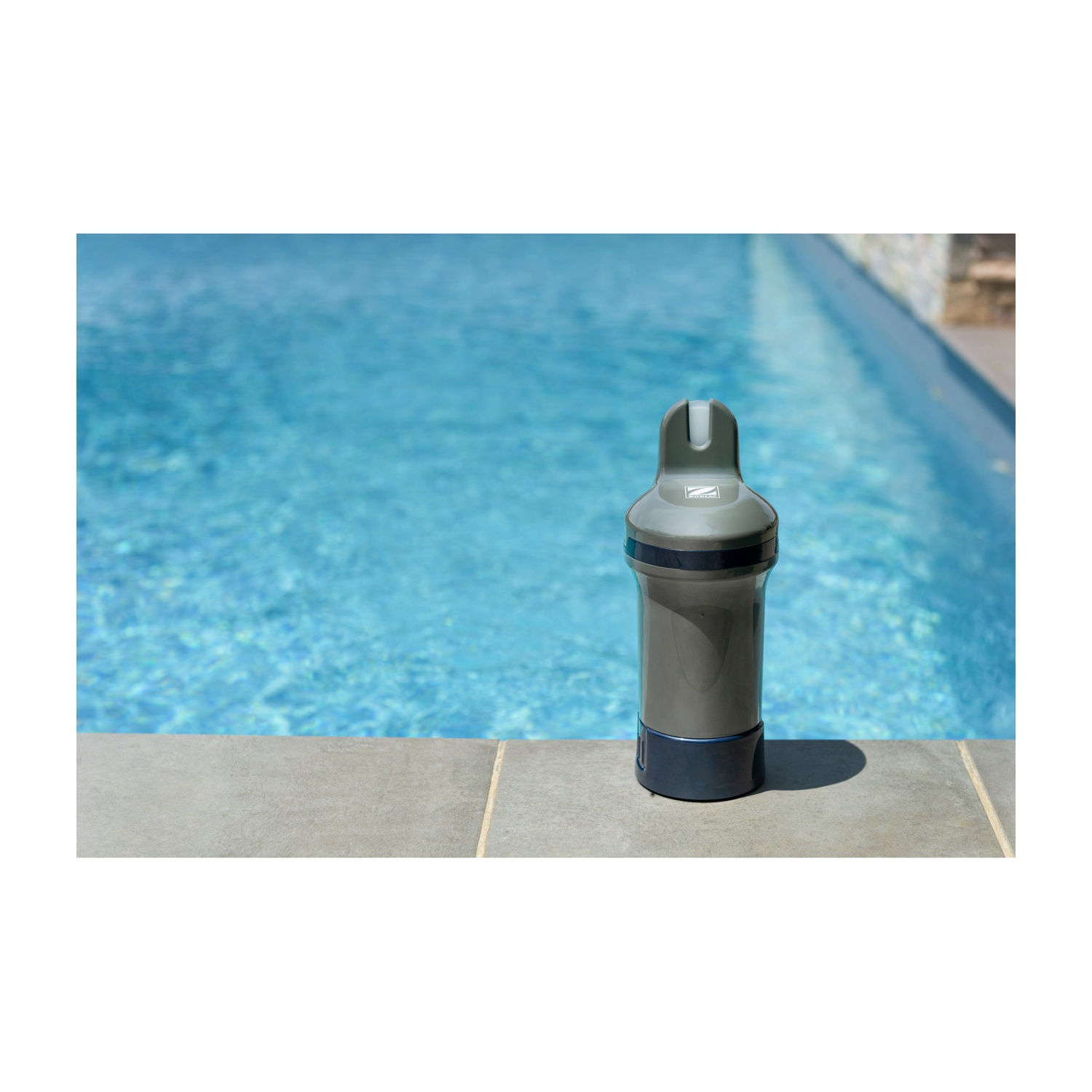 Un dispositivo cilindrico grigio con base blu scuro si trova vicino a una piscina blu brillante.