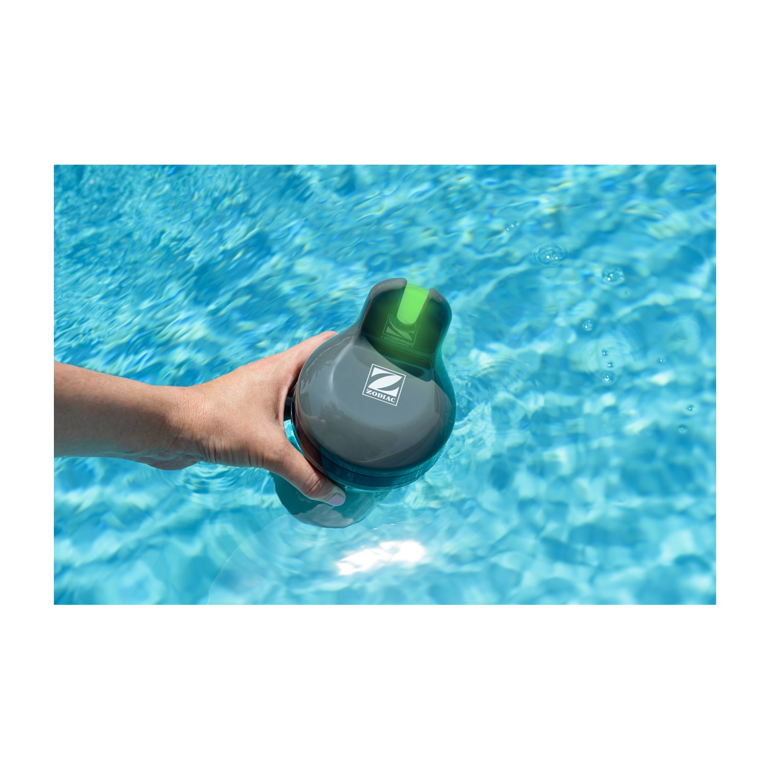 Una mano tiene un pulitore per piscina grigio con parte superiore verde nell'acqua blu.