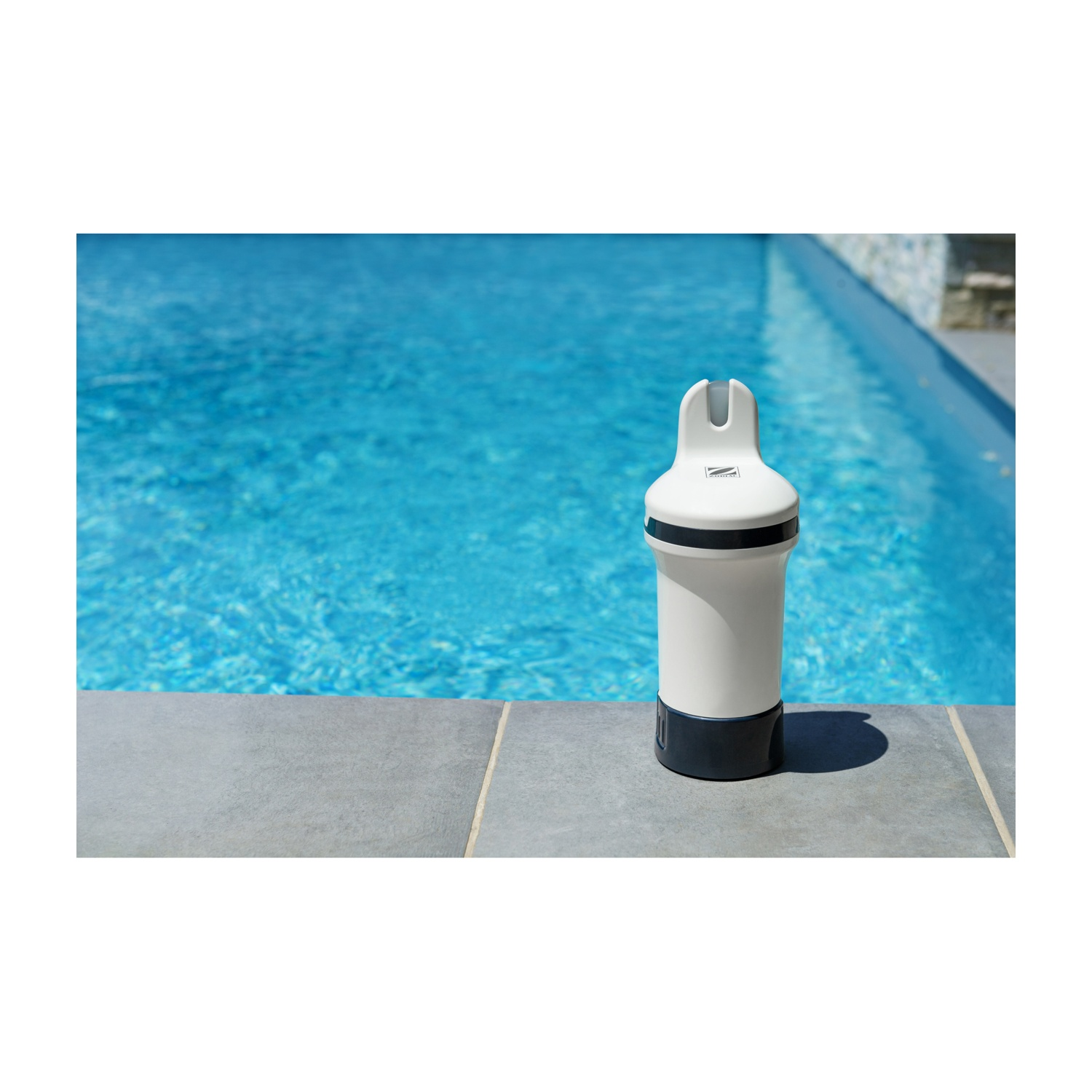 Un pulitore per piscina bianco e grigio scuro sul bordo piscina accanto a una piscina blu.