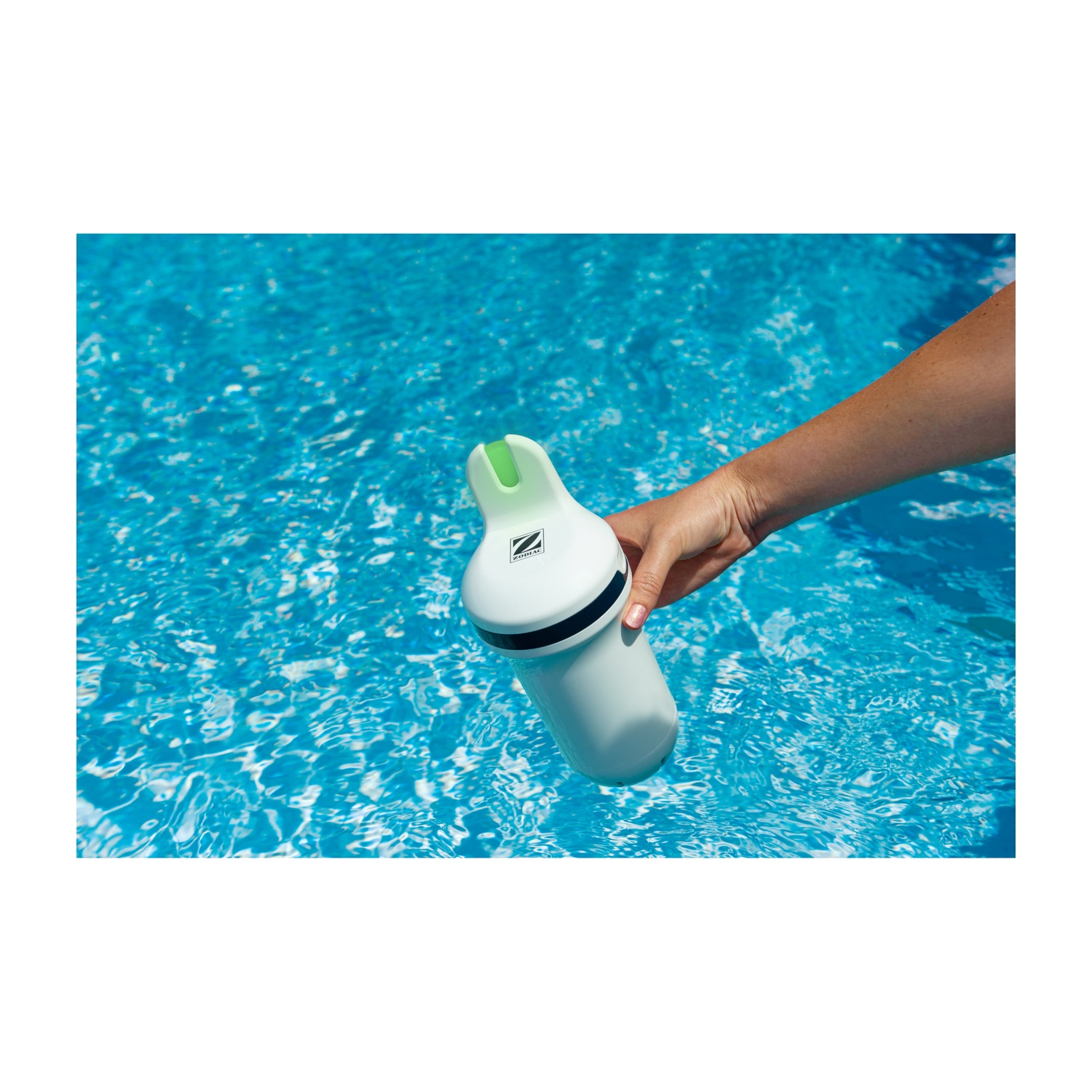 Una mano tiene un pulitore per piscina bianco con accento verde sull'acqua blu.