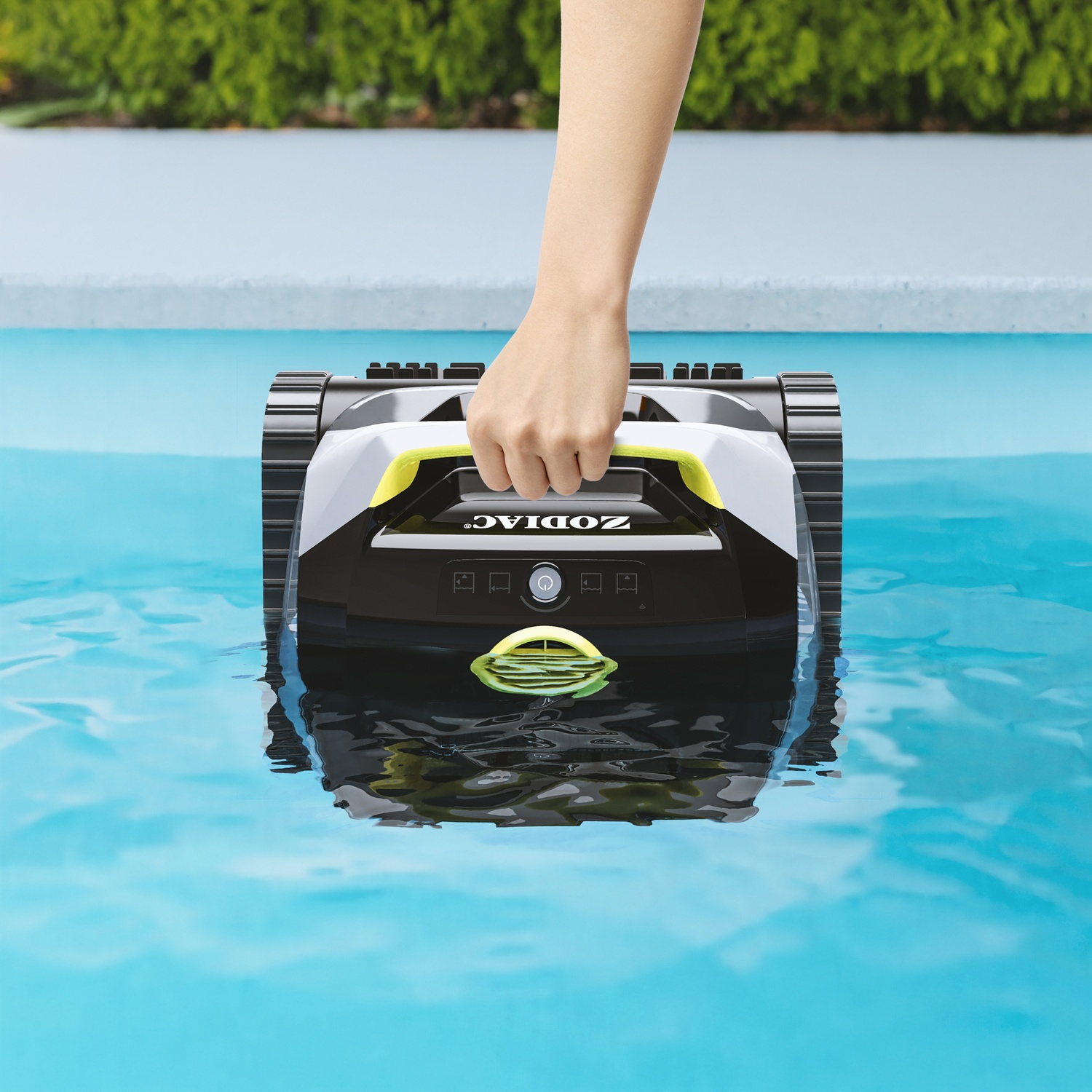Una mano posiziona un robot pulitore nero e giallo in acqua blu brillante.