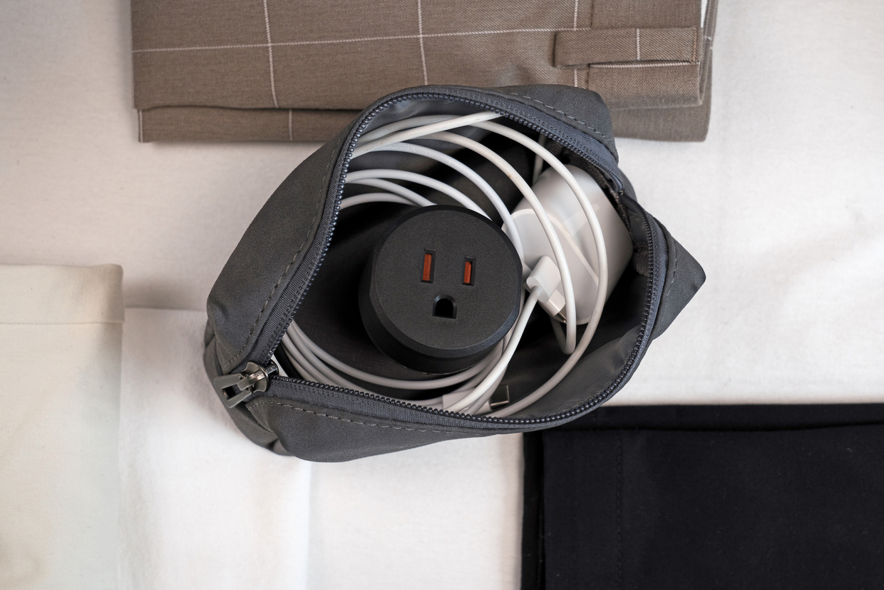 Grauer Beutel mit weißen Kabeln und einem schwarzen Netzstecker-Adapter.