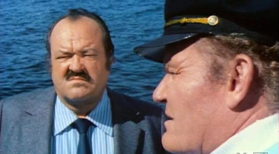 Zwei Männer auf einem Boot mit blauem Wasser im Hintergrund.