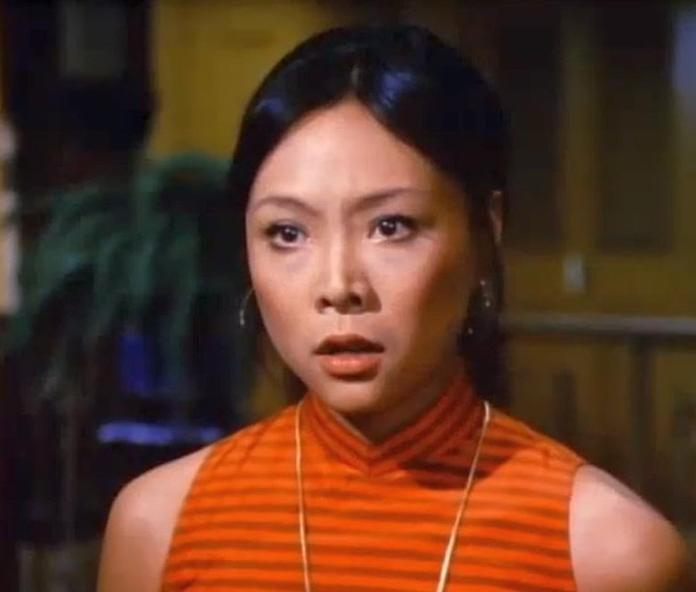 Eine Frau mit dunklem Haar trägt ein orange gestreiftes Kleid mit hohem Kragen.
