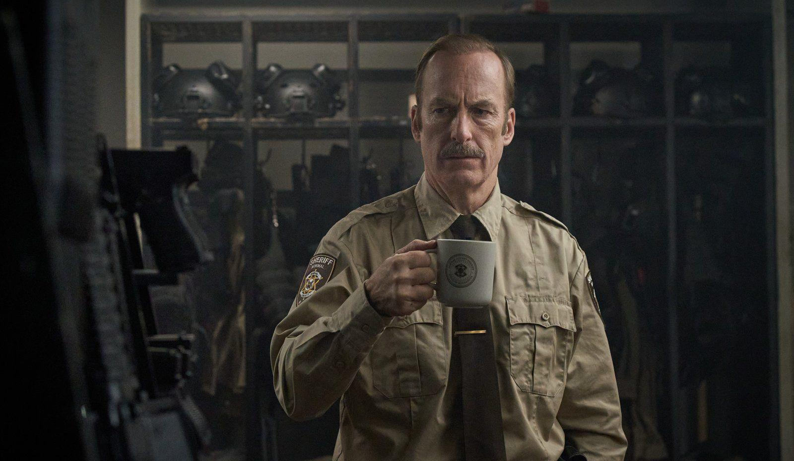 Ein Sheriff in Uniform hält einen Becher, im Hintergrund Schließfächer und Helme.