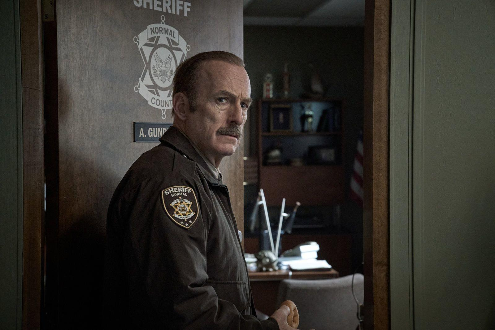 Ein Mann in Sheriff-Uniform steht vor einer Tür mit einem Sheriff-Abzeichen.