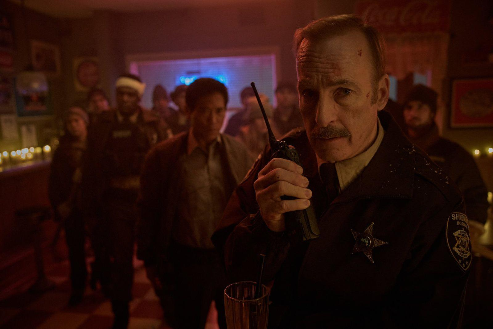 Ein Mann in Sheriff-Uniform hält ein Funkgerät in einer schwach beleuchteten Bar.