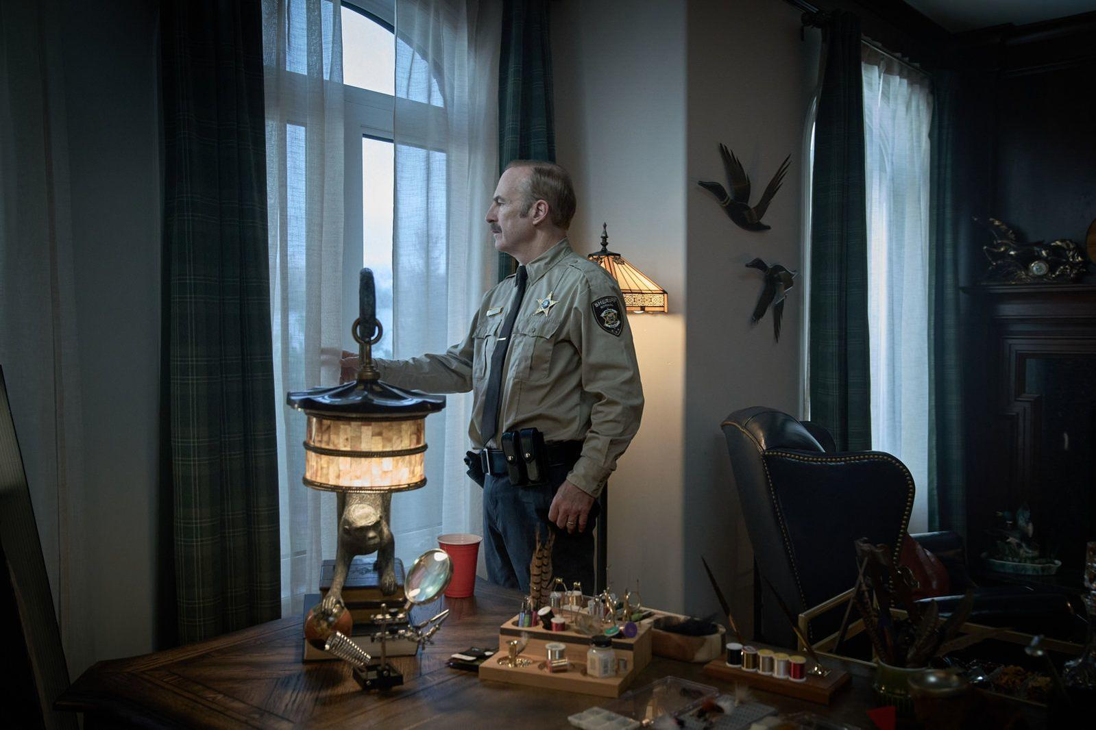 Ein Mann in Sheriff-Uniform steht neben einem Fenster und berührt eine Lampe.
