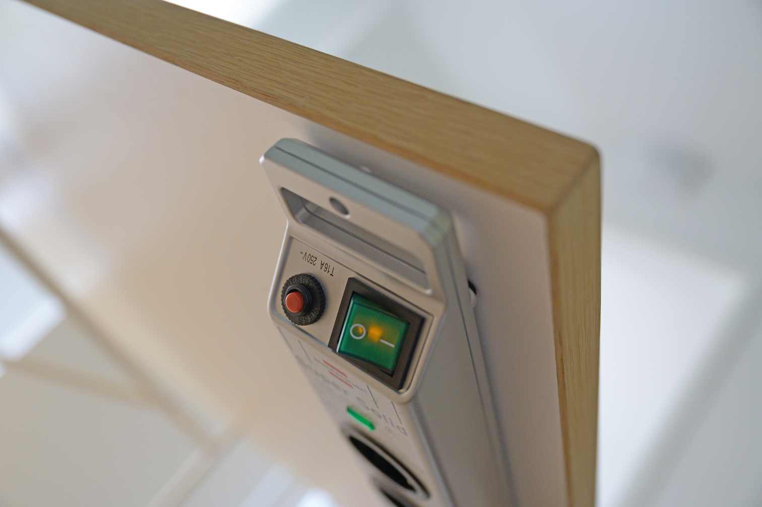 Eine weiße Steckdosenleiste mit grünem Schalter und rotem Knopf an einem Holztisch.