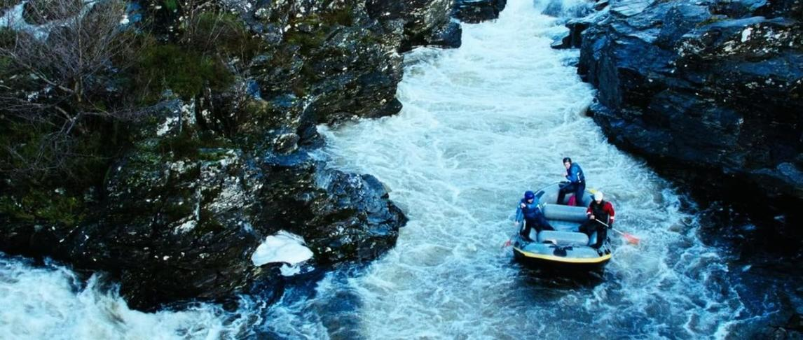 Ein Floß mit vier Personen navigiert zwischen felsigen Klippen durch reißende Stromschnellen.