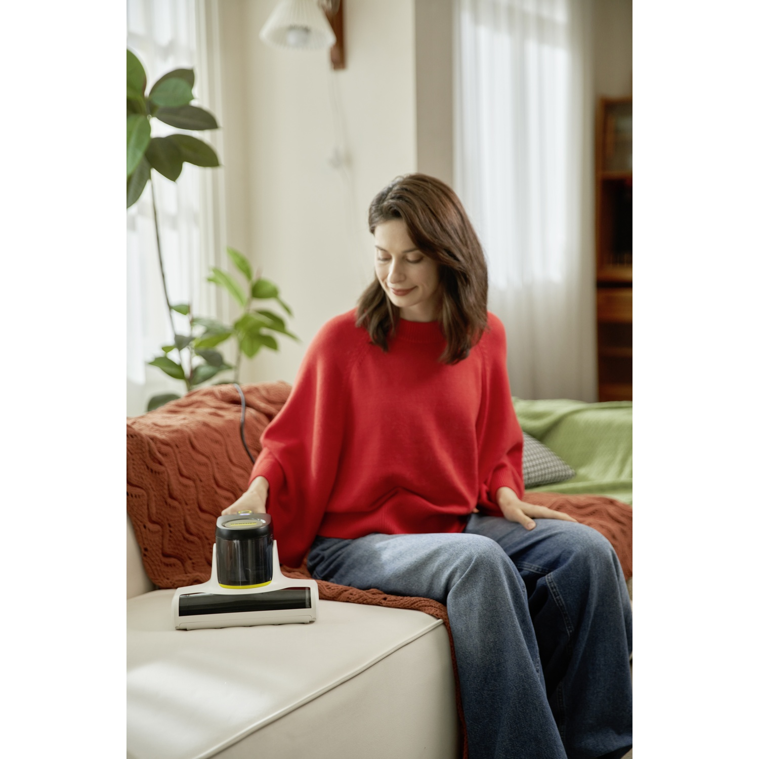 Donna in maglione rosso e jeans usa aspirapolvere portatile.