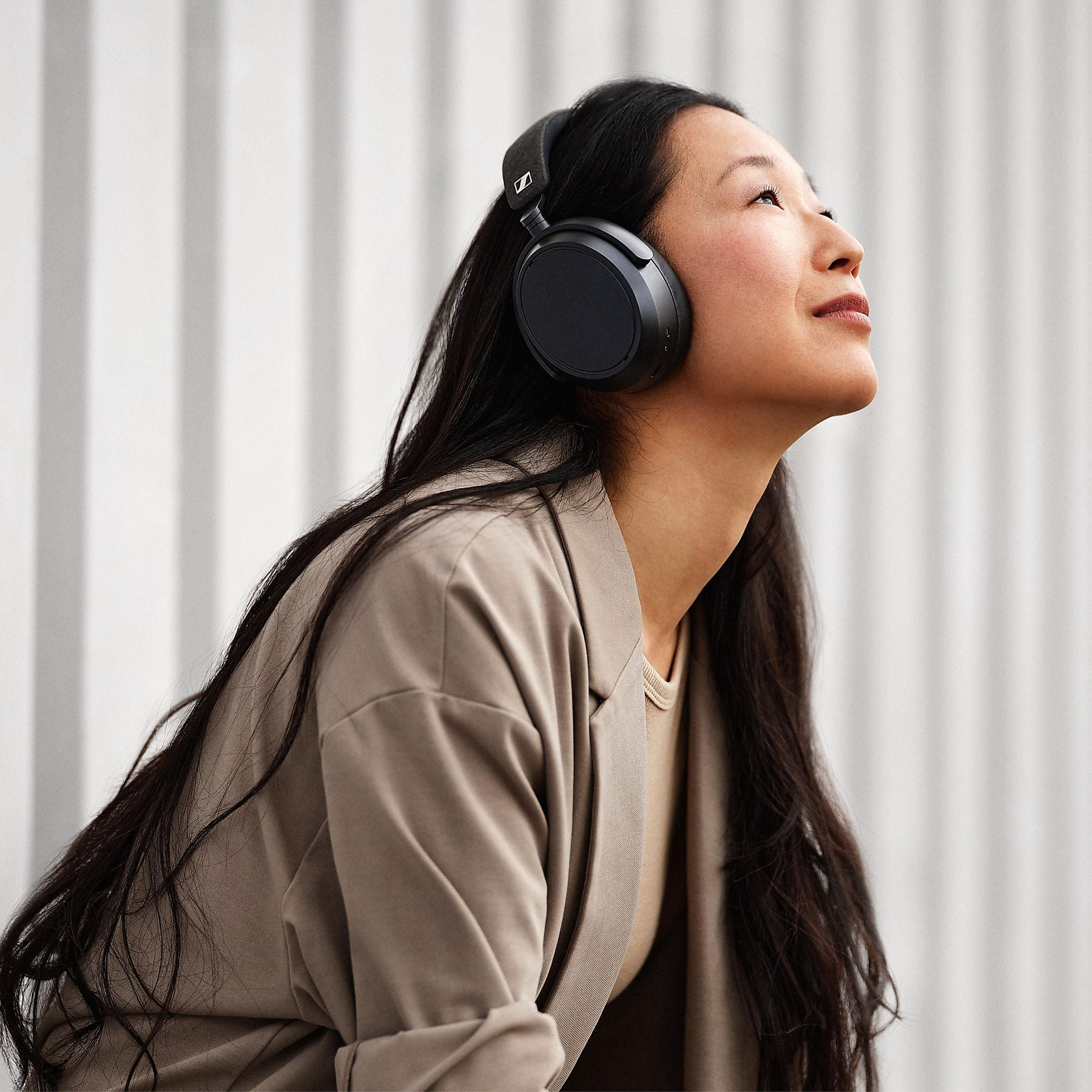 Mujer con auriculares mira hacia arriba, vistiendo un blazer beige.