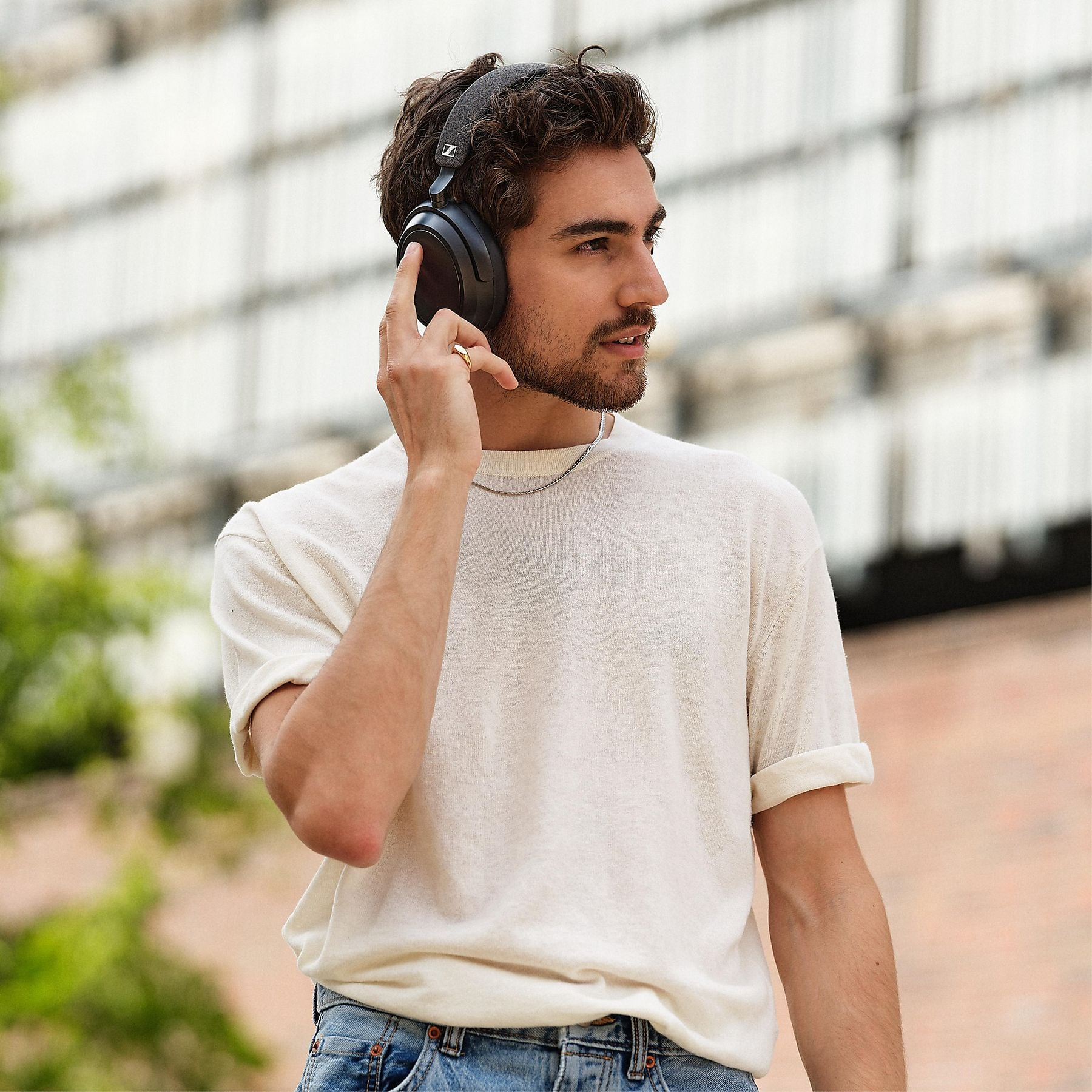 Un hombre con auriculares se toca la oreja, viste camisa blanca y jeans.