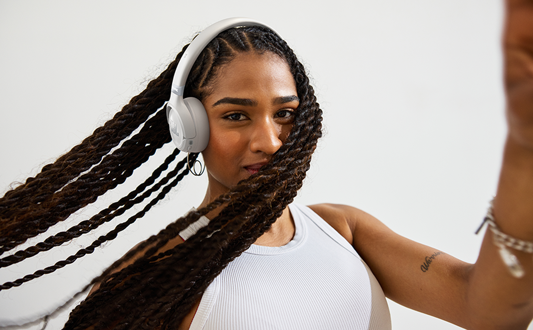 Mujer con auriculares blancos y trenzas largas y castañas, girando ligeramente.