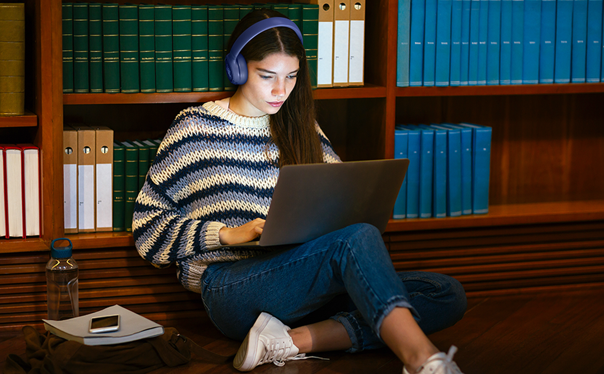 Una joven con auriculares se sienta en el suelo usando una laptop.