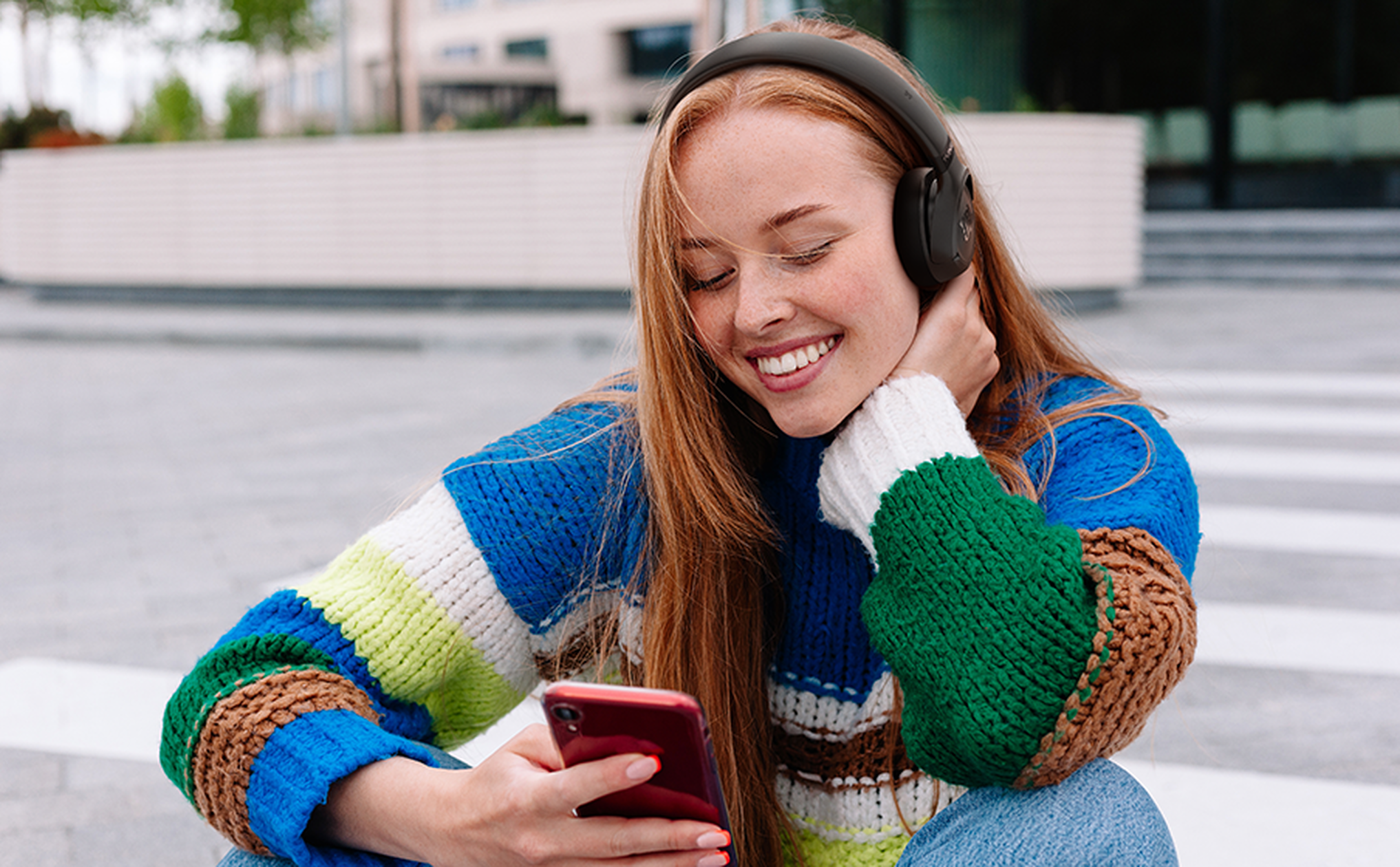 Una joven con auriculares y un teléfono inteligente sonríe.