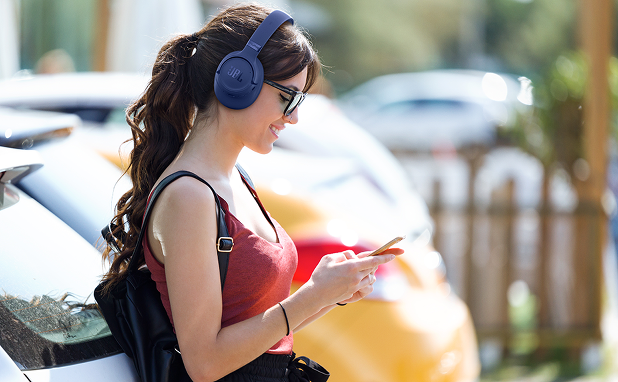 Mujer con auriculares y teléfono se apoya en un coche.