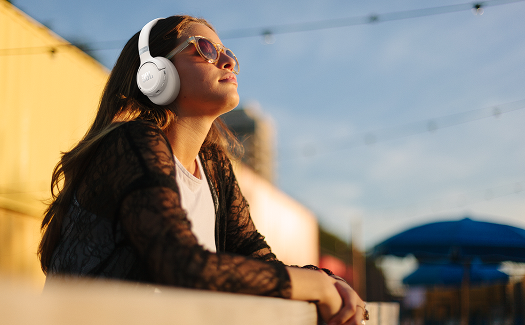 Una joven con auriculares y gafas de sol mira hacia arriba.